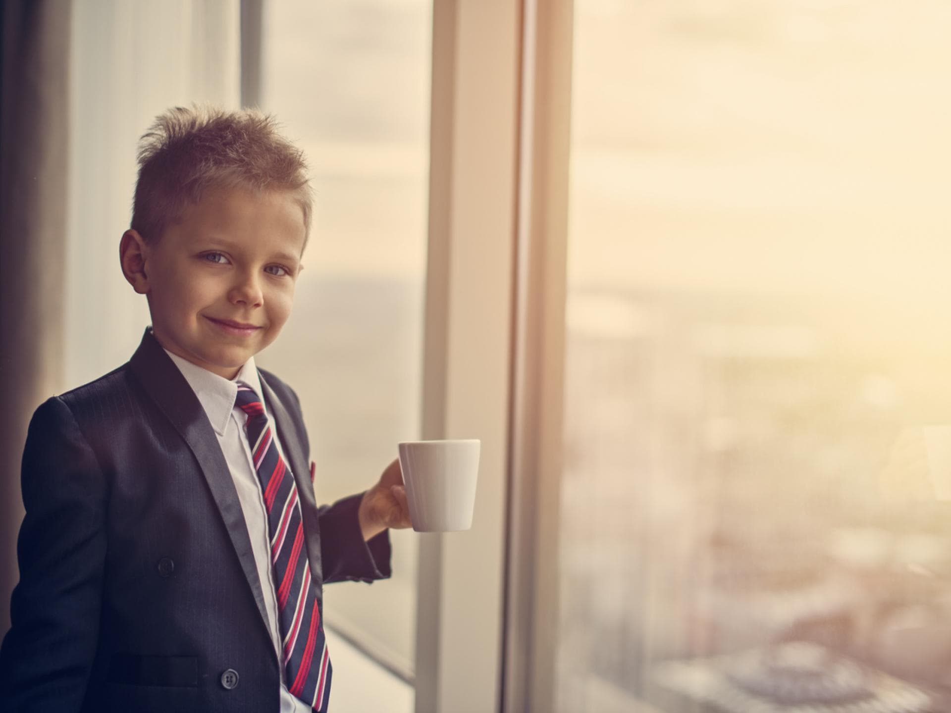 Ein Junge steht im Anzug am Fenster mit einer Kaffeetasse. Ein Junge steht im Anzug am Fenster mit einer Kaffeetasse.