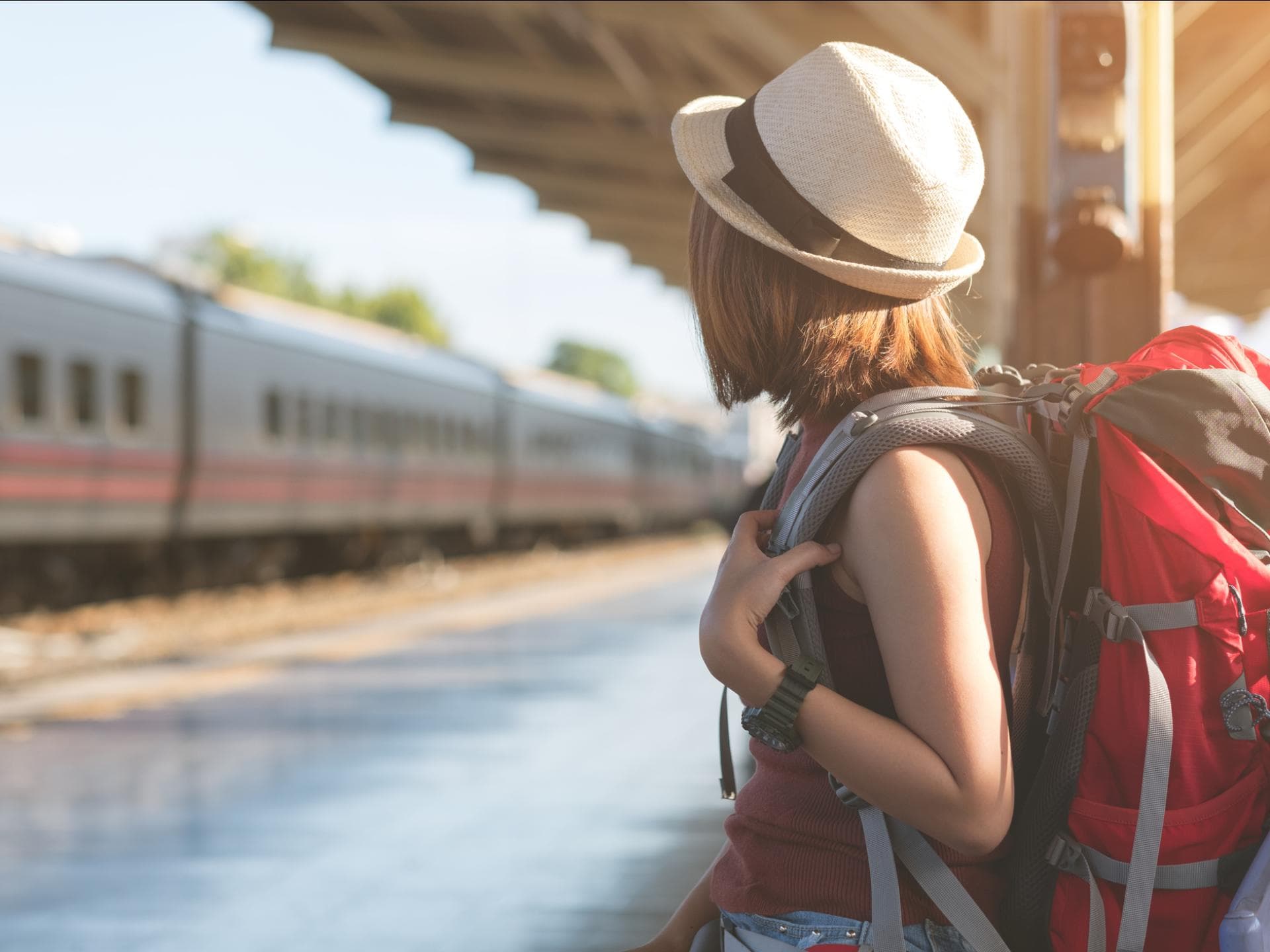 Ein junges Mädchen steht mit einem Rucksack an einem Bahngleis und wartet.