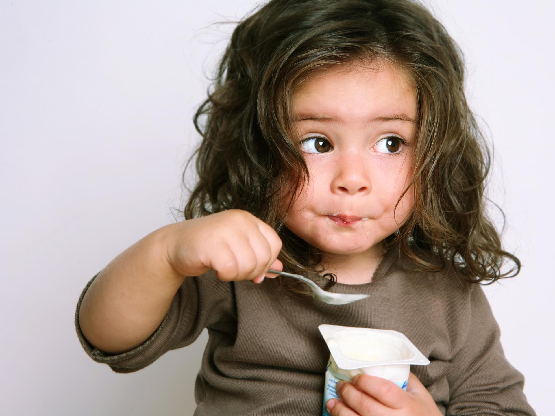 Fruchtjoghurts enthalten mehr Zucker, als man denkt. Kleinkind löffelt einen Joghurt.