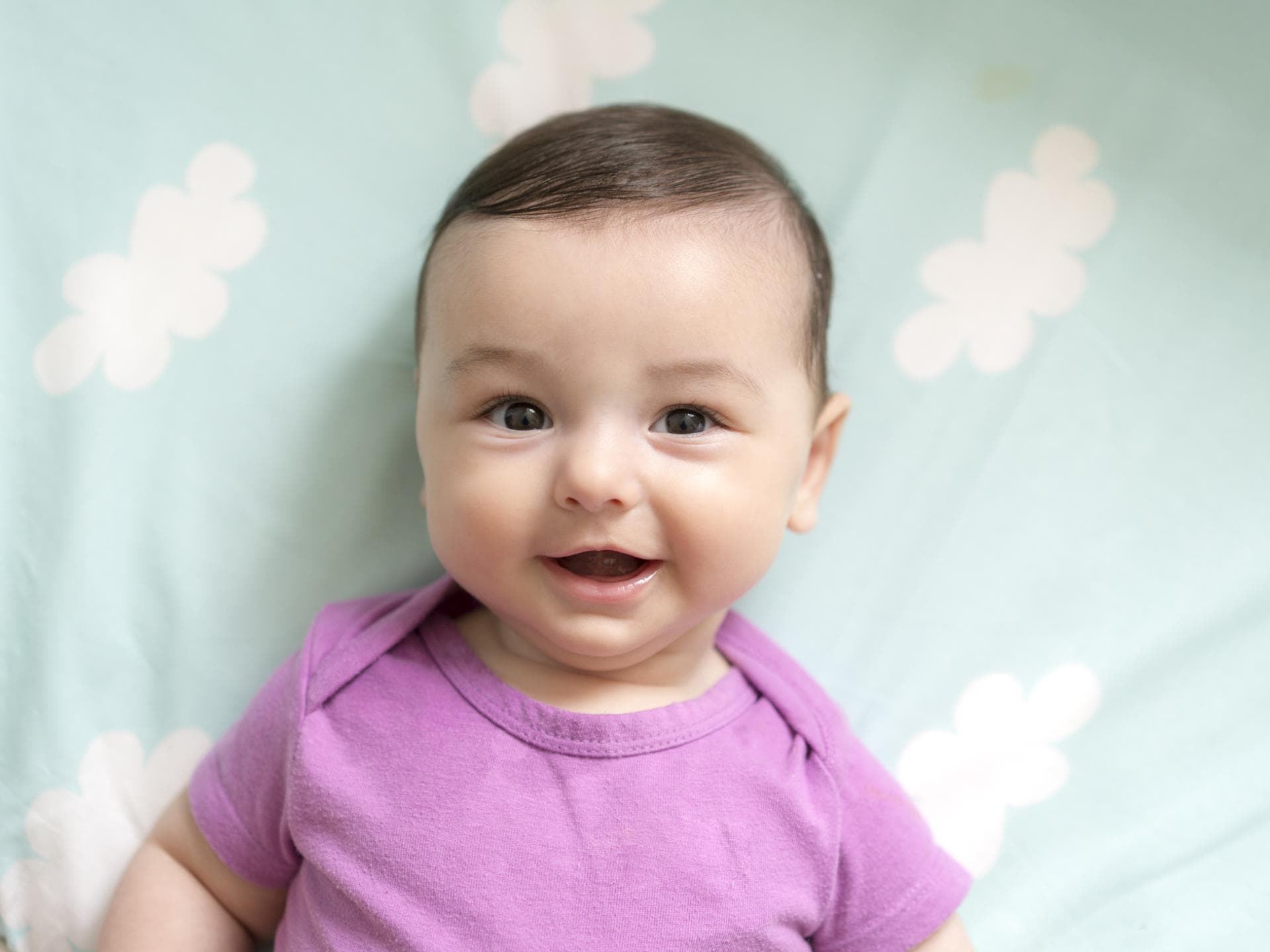 Ein Baby liegt lächelnd auf einer Decke mit kleinen Wolken. 