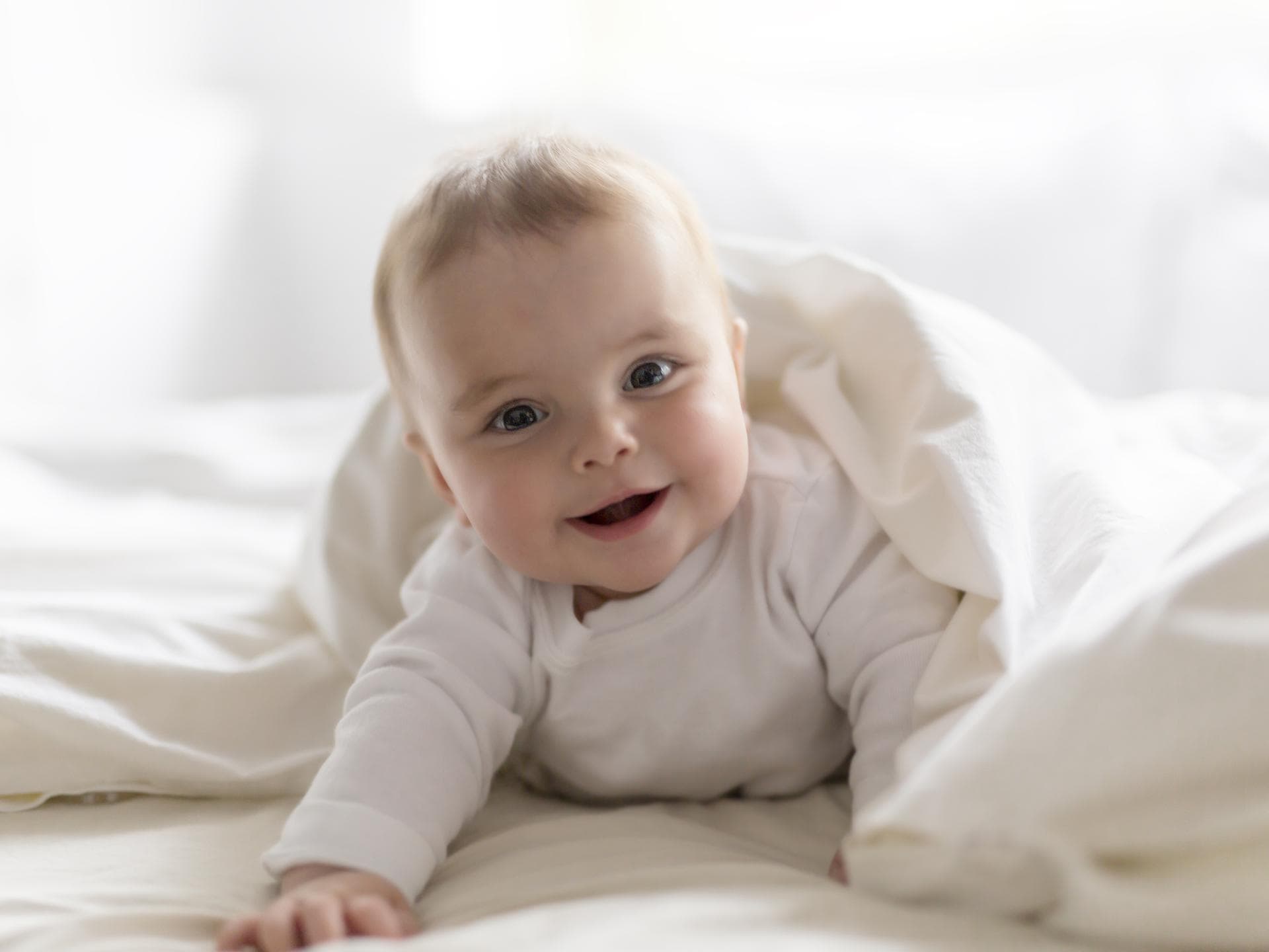 Ein Baby liegt lächelnd im Bett.