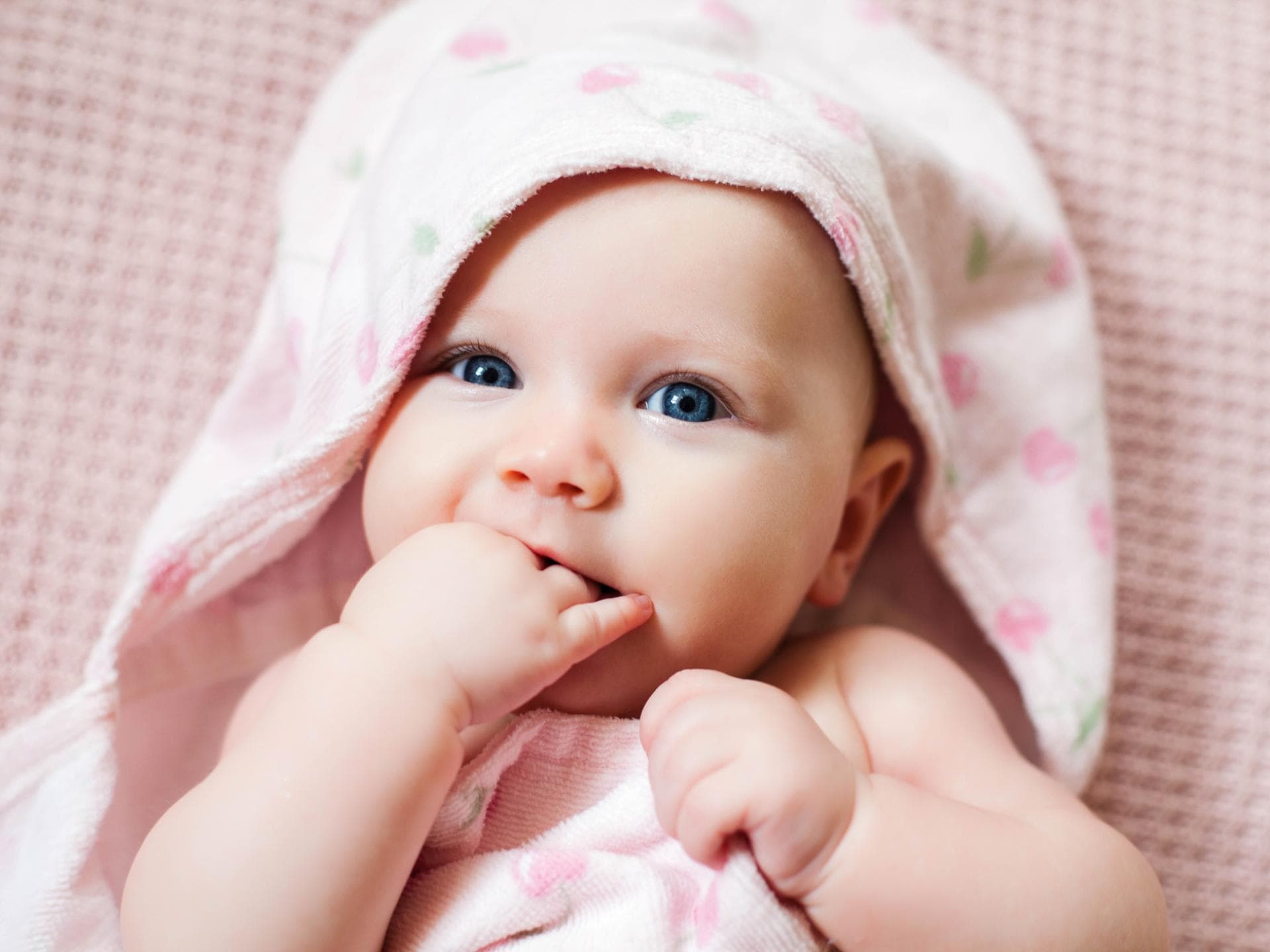 Ein kleines Baby liegt in rosa Bademantel auf einem Tuch.