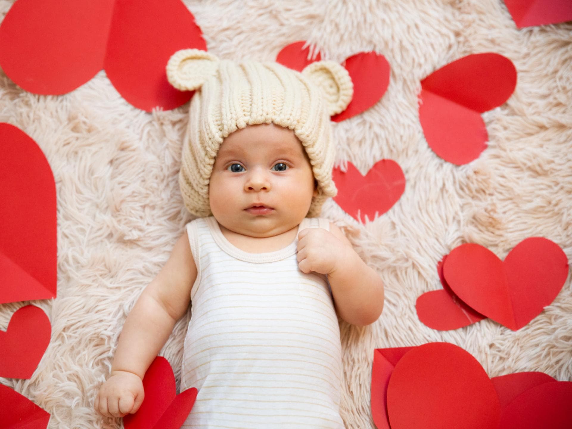 Ein Baby liegt umringt von Papierherzen auf einem Teppich.