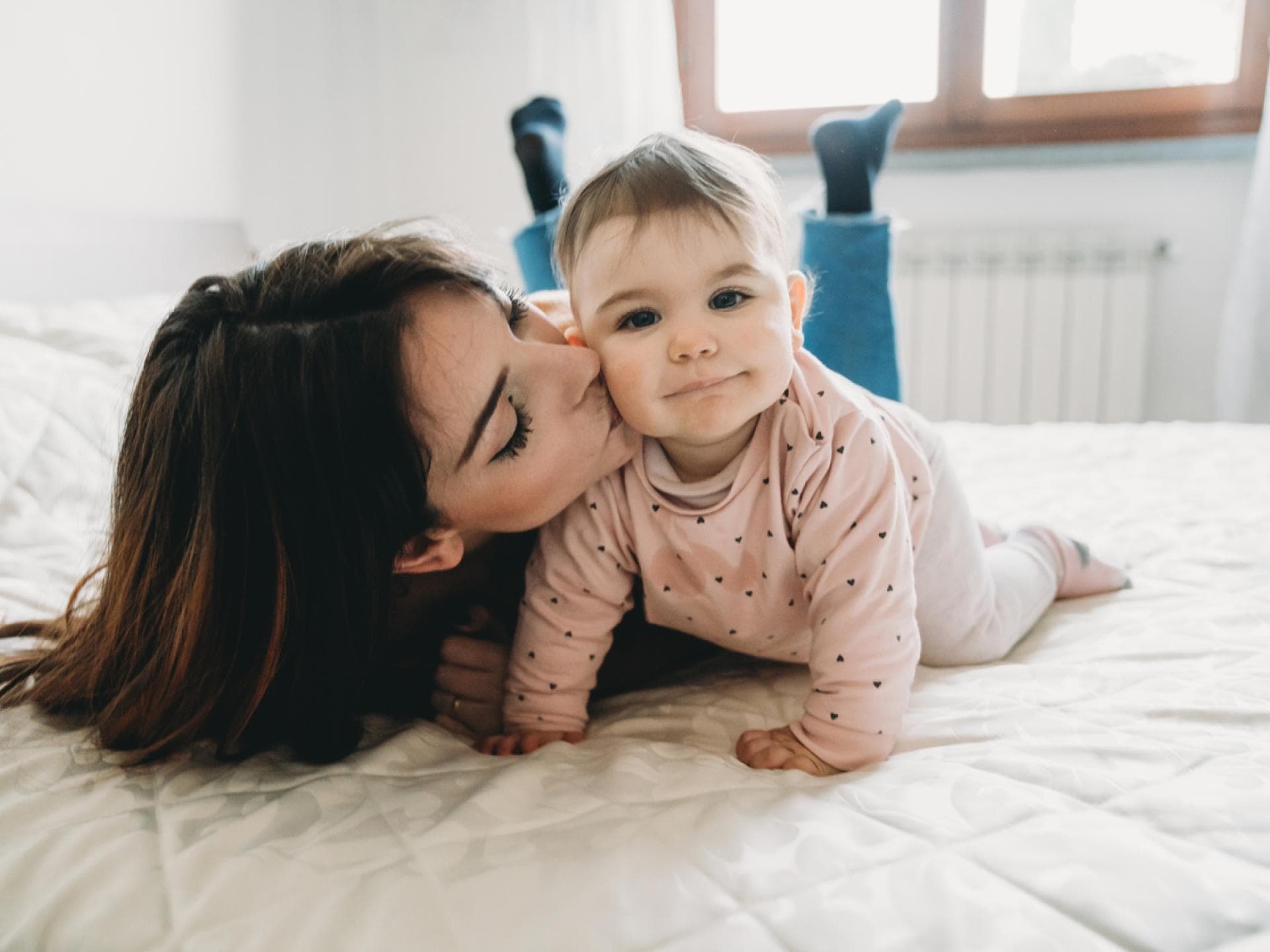 Eine junge Mutter küsst ihre kleine Baby-Tochter auf die Wange.