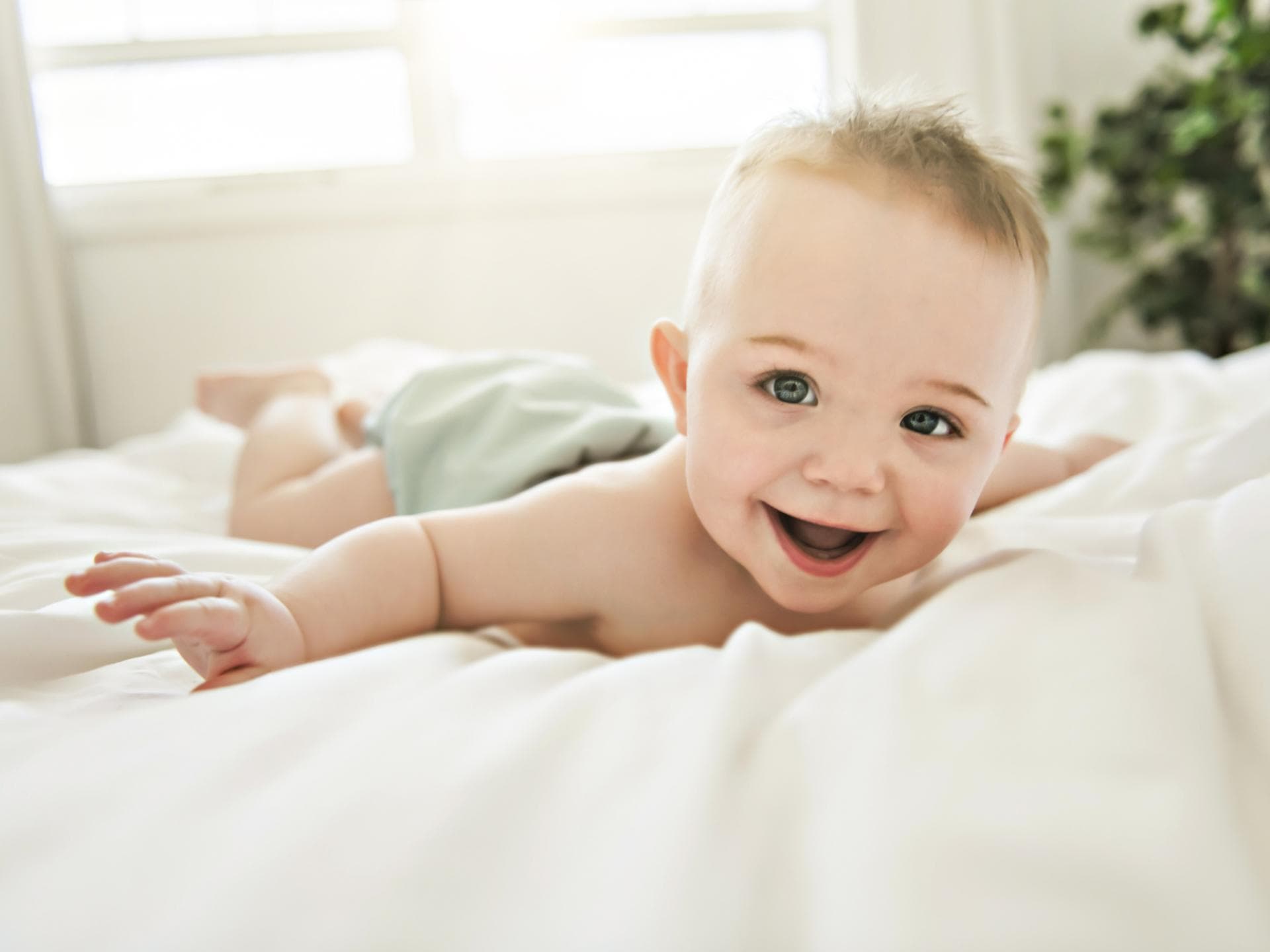 In diesen Artikel gibt es außergewöhnliche Jungennamen mit U zu entdecken. Ein kleiner junge liegt lachend auf dem Bett.