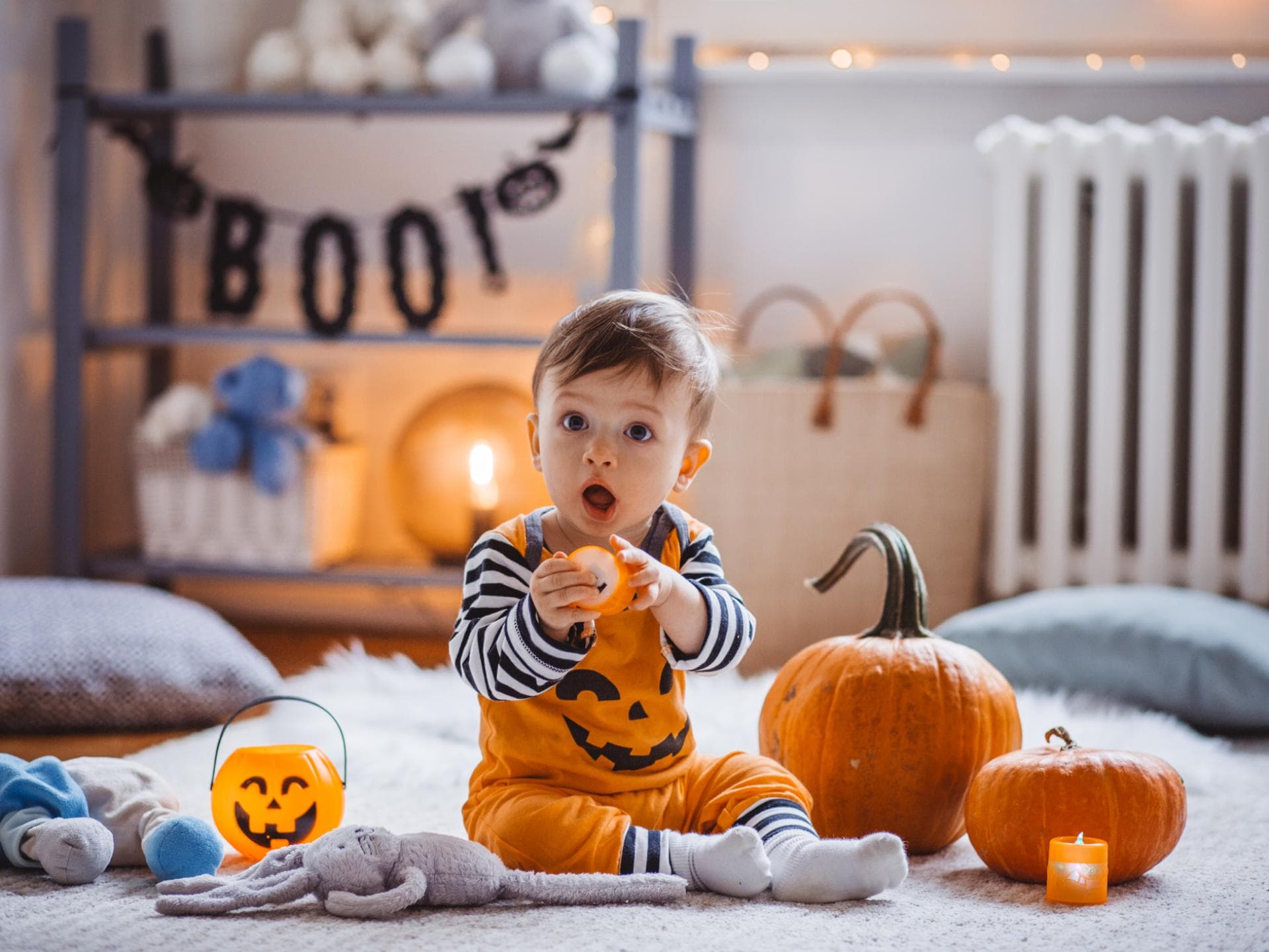 Oktober-Babys sind oft kreativ, unkompliziert und diplomatisch. Ein kleiner Junge sitzt als Kürbis verkleidet zwischen Halloween-Dekoration.