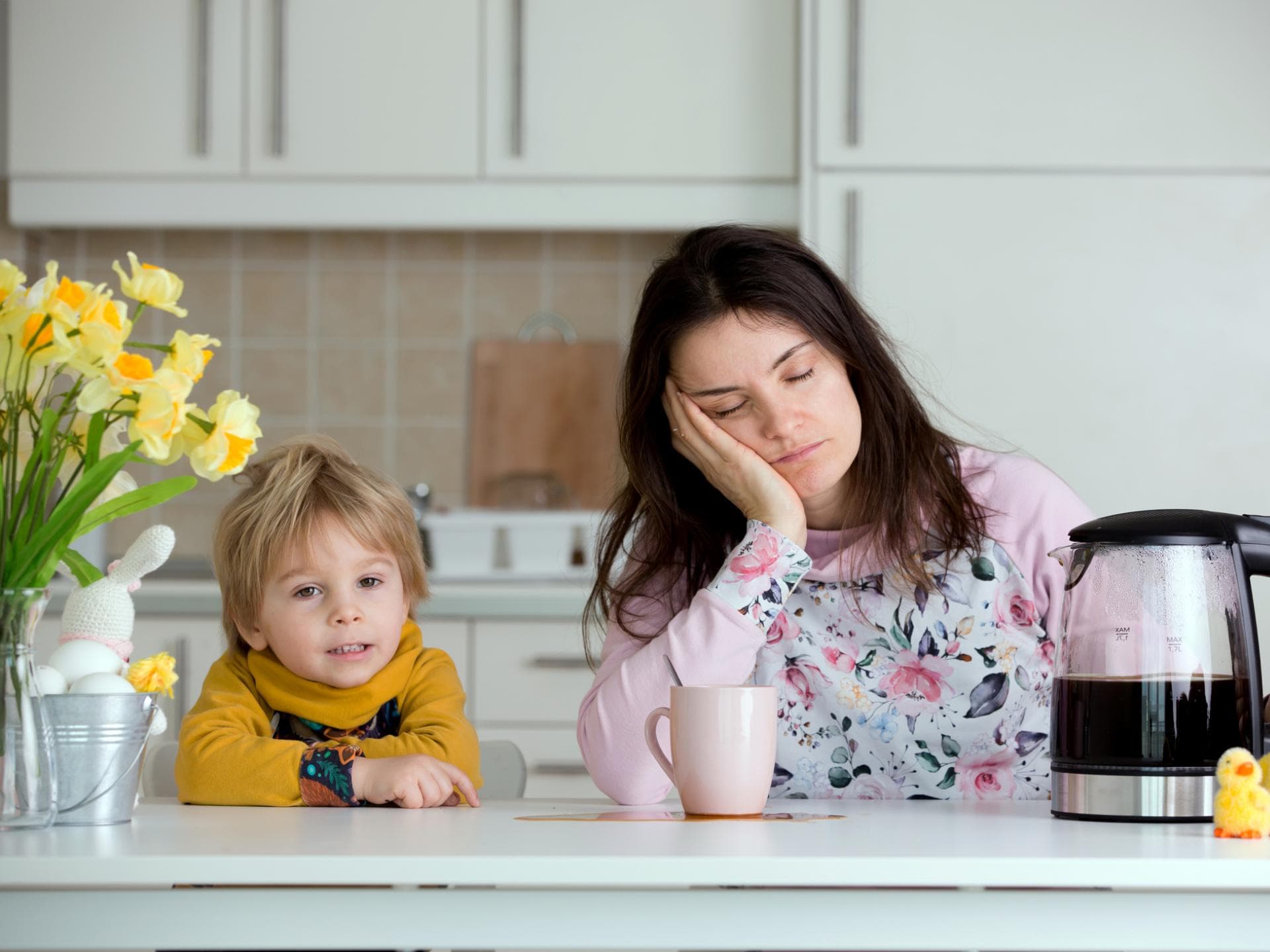 Mama sitzt müde am Tisch, Kind ist hellwach