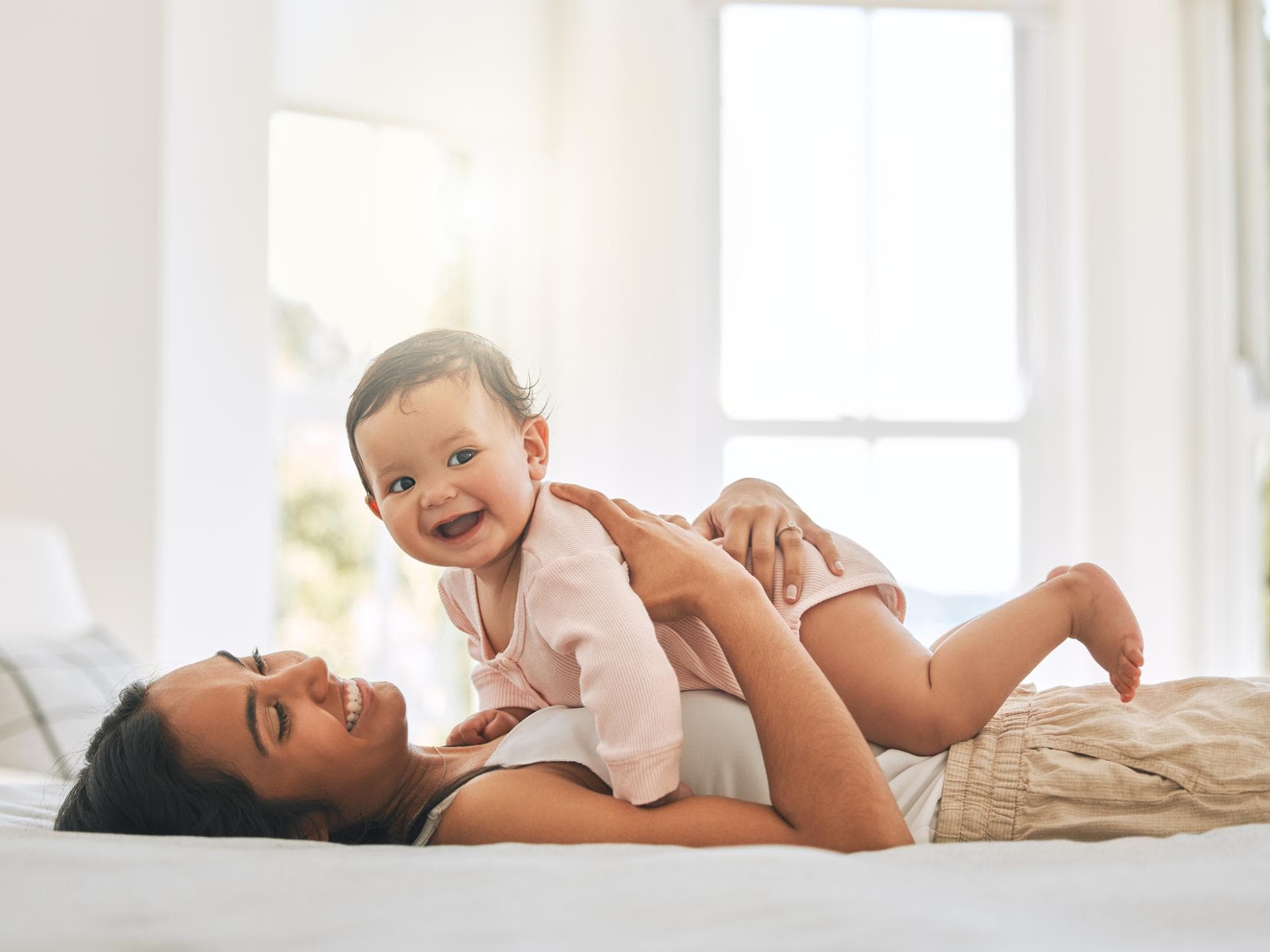 In diesem Artikel gibt es Mädchennamen mit N für euch zu entdecken. Ein Baby liegt lachend auf dem Bauch seiner Mama.