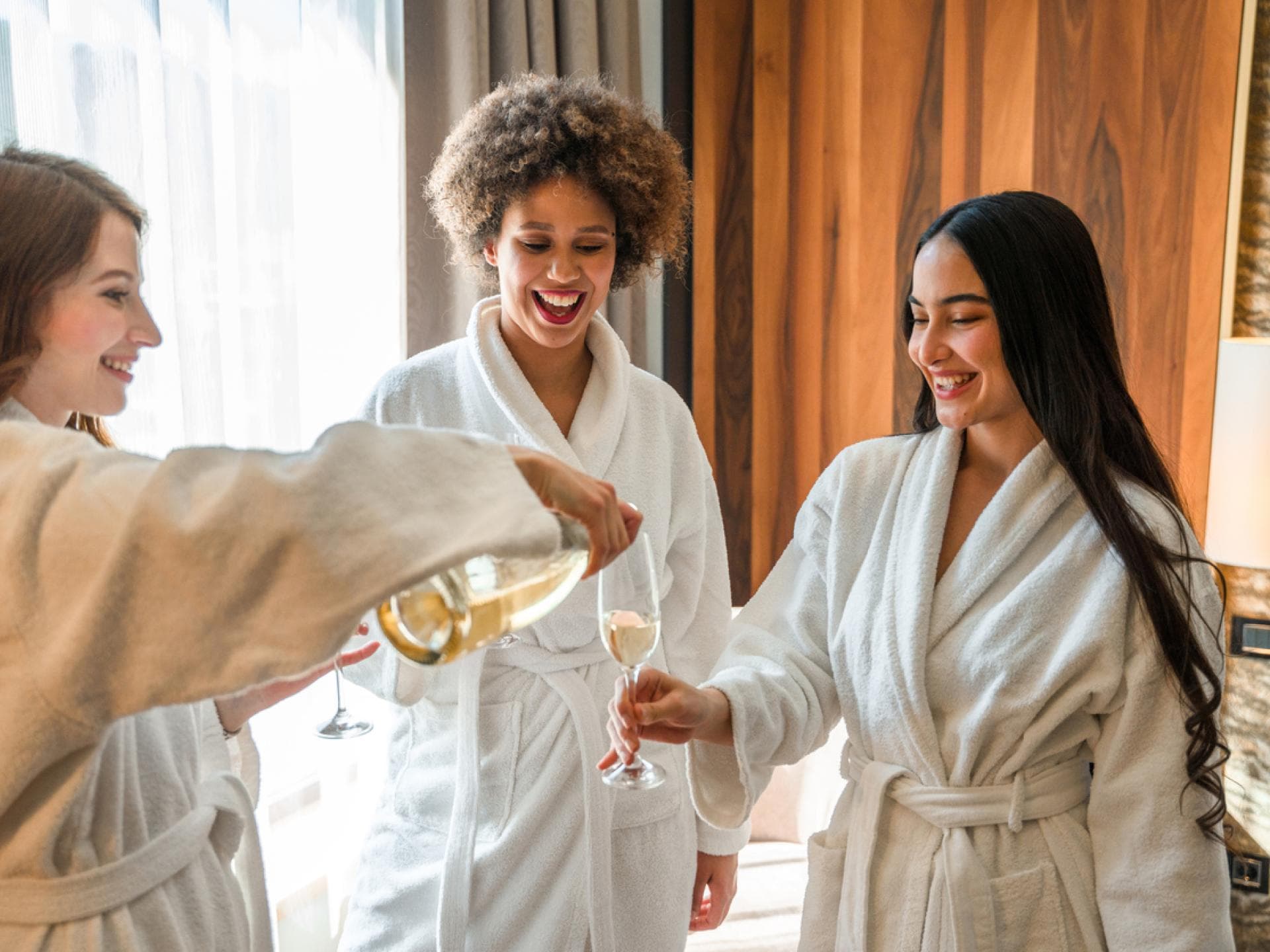 Spa-Day: Drei Freundinnen schenken sich Sekt im Wellness-Bademantel ein