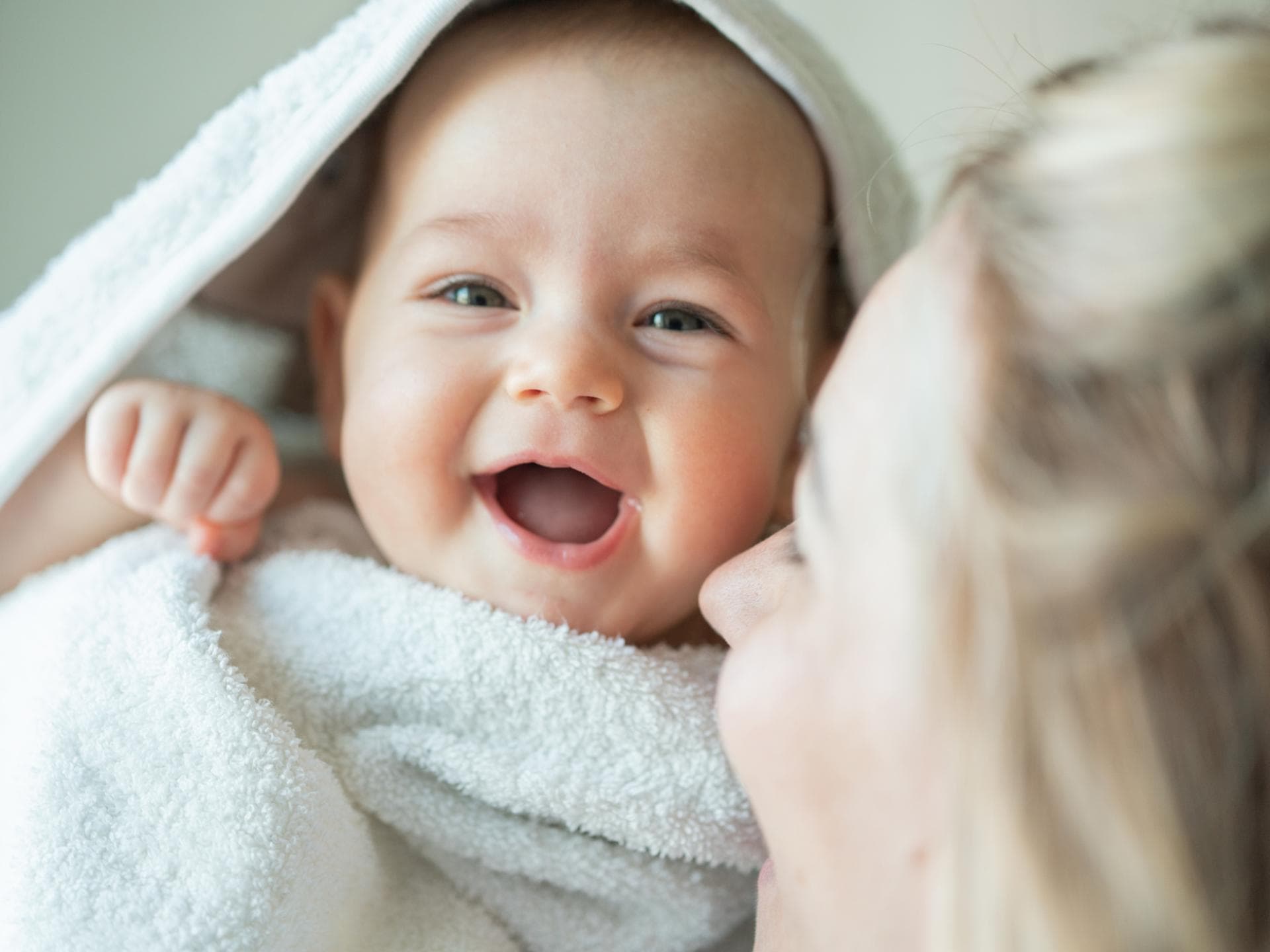 Mädchennamen mit L sind oft klangvoll und beliebt. Ein Baby ist in ein Handtuch eingewickelt und lacht.