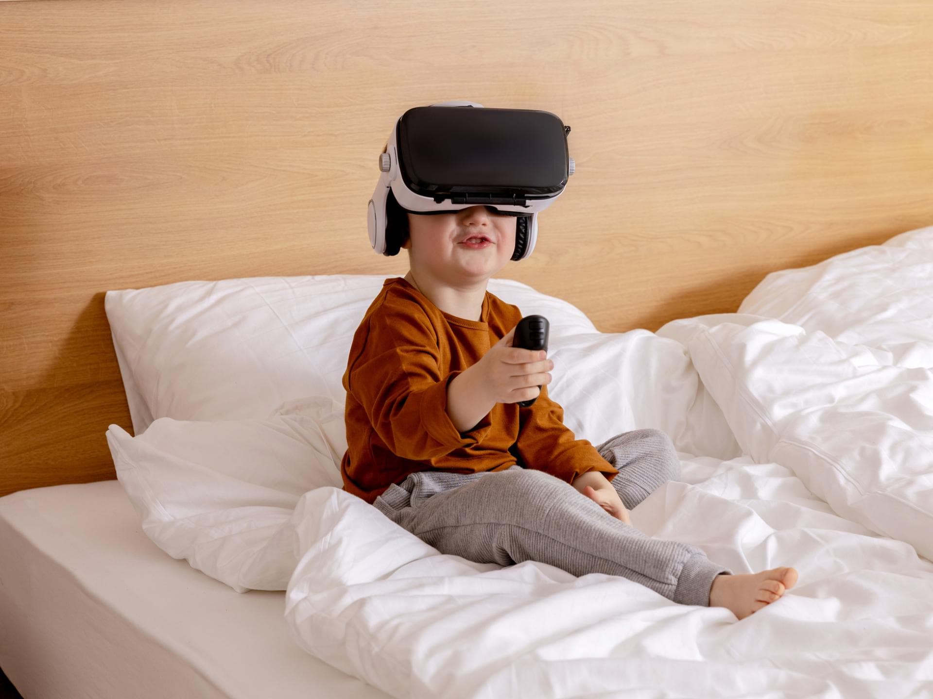 Ein kleiner Junge sitzt auf dem Bett und hat eine VR-Brille auf.