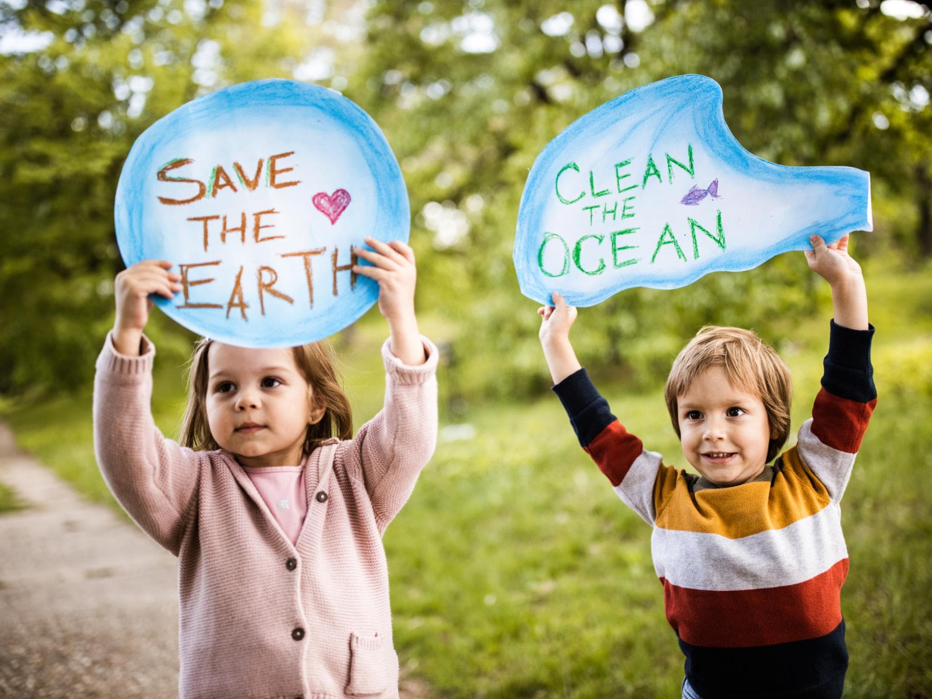 Kinderbücher zum Klimaschutz helfen schon den Kleinen, das Thema Klimawandel zu verstehen. Ein Mädchen und ein Junge halten Schilder mit der Aufschrift "Save the Earth" und "Clean the Ocean".