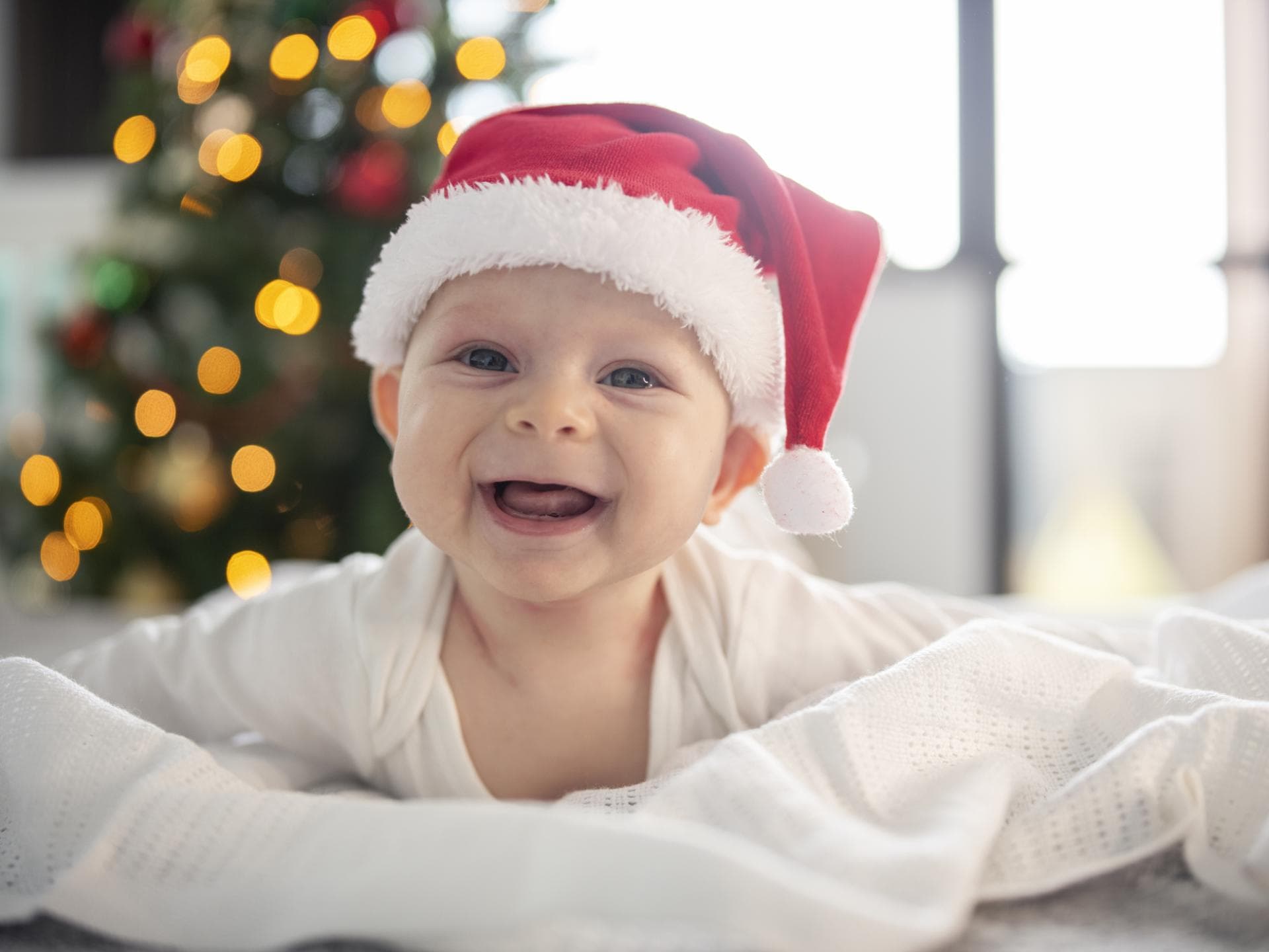 Ein Baby hat eine Weihnachtsmütze auf und lacht.