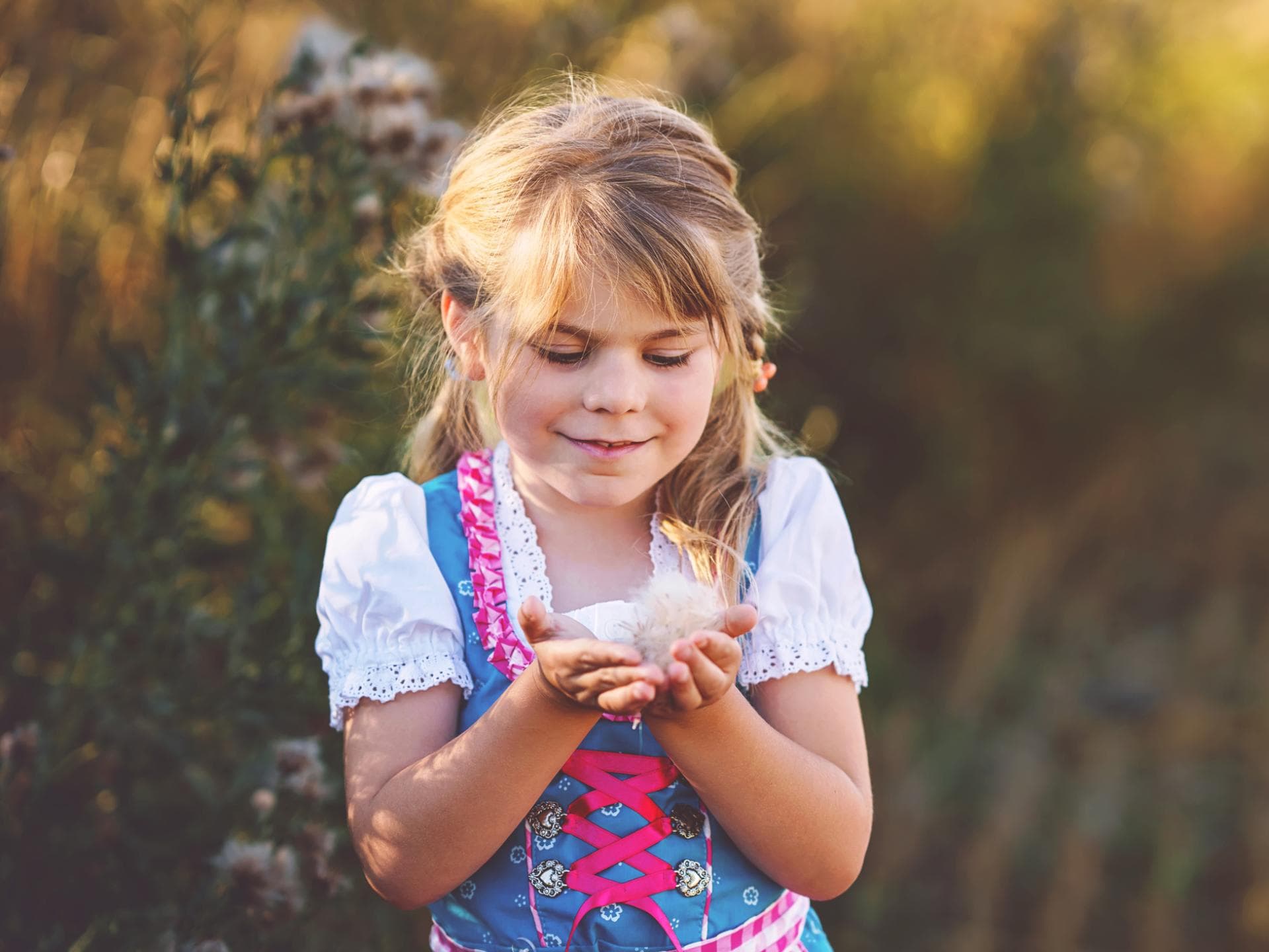 Bayerische Mädchennamen sind vielseitig. Ein kleines Mädchen im Dirndl steht auf dem Feld und hält eine Blüte in der Hand.