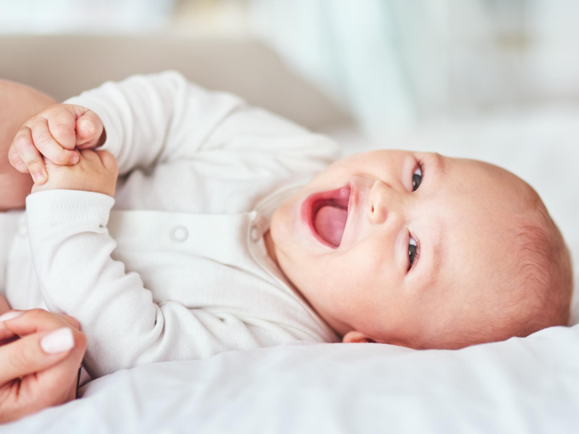 Von Oscar bis Otis: In unserer Übersicht haben wir viele Jungennamen mit O zusammengetragen. Ein kleines Baby liegt lachend auf dem Bett.