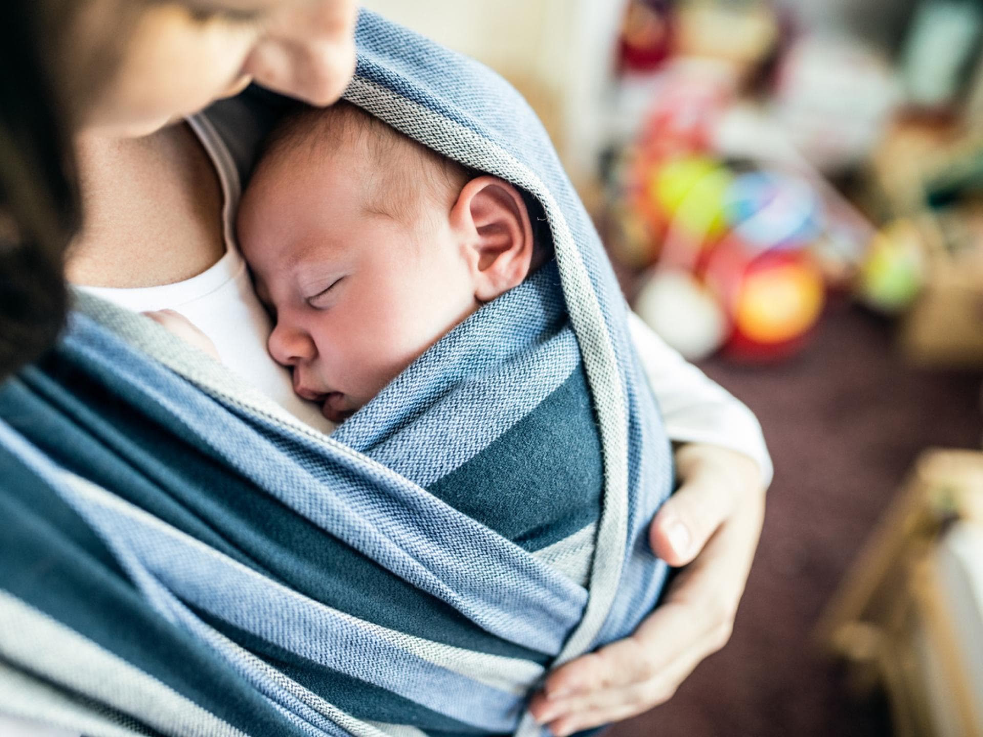 Baby im Tragetuch vor der Brust seiner Mutter.