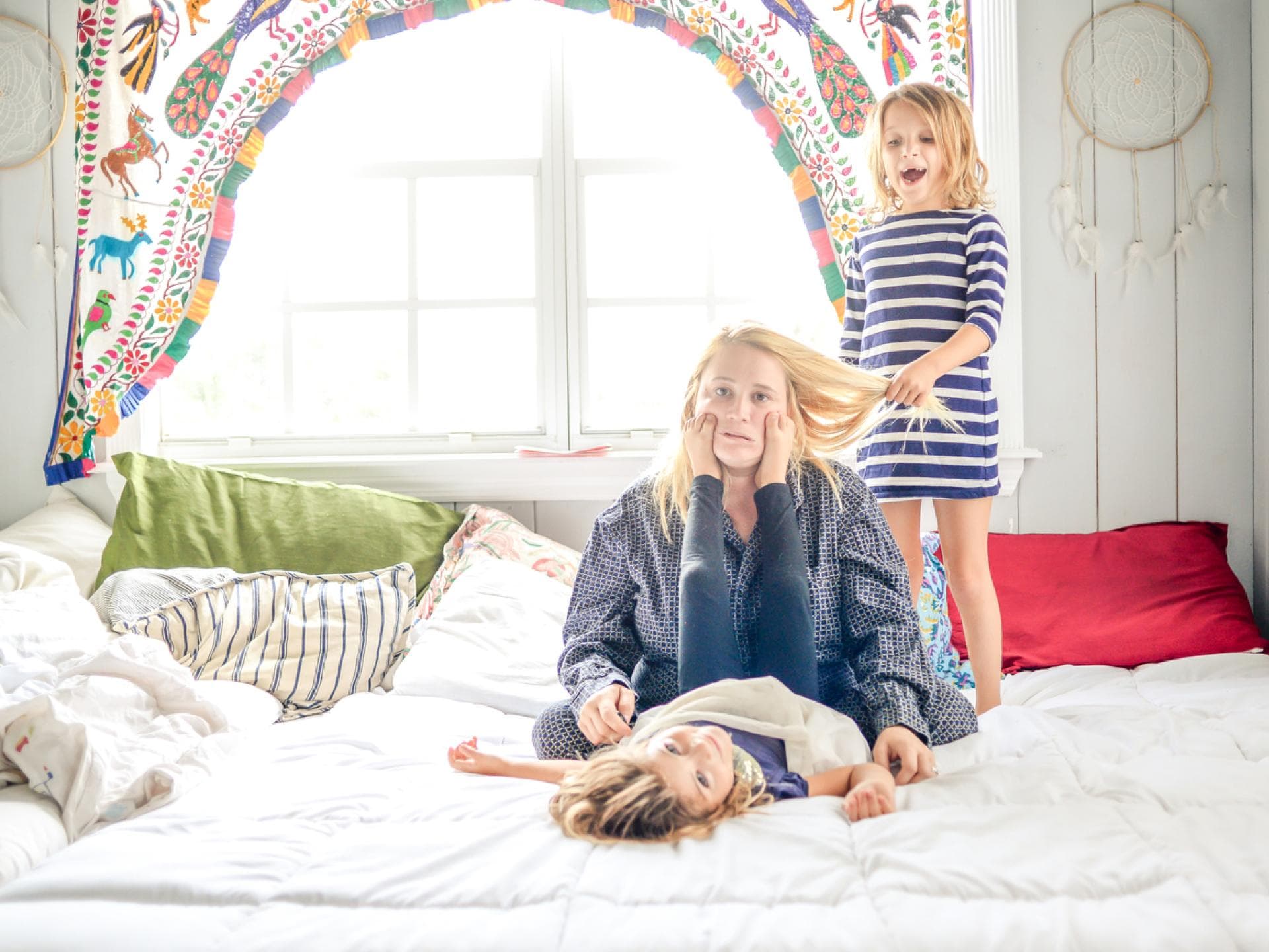 Ausgelaugte Mutter sitzt auf Bett, Kinder ziehen an ihren Haaren und machen Quatsch. Ausgelaugte Mutter sitzt auf Bett, Kinder ziehen an ihren Haaren und machen Quatsch.