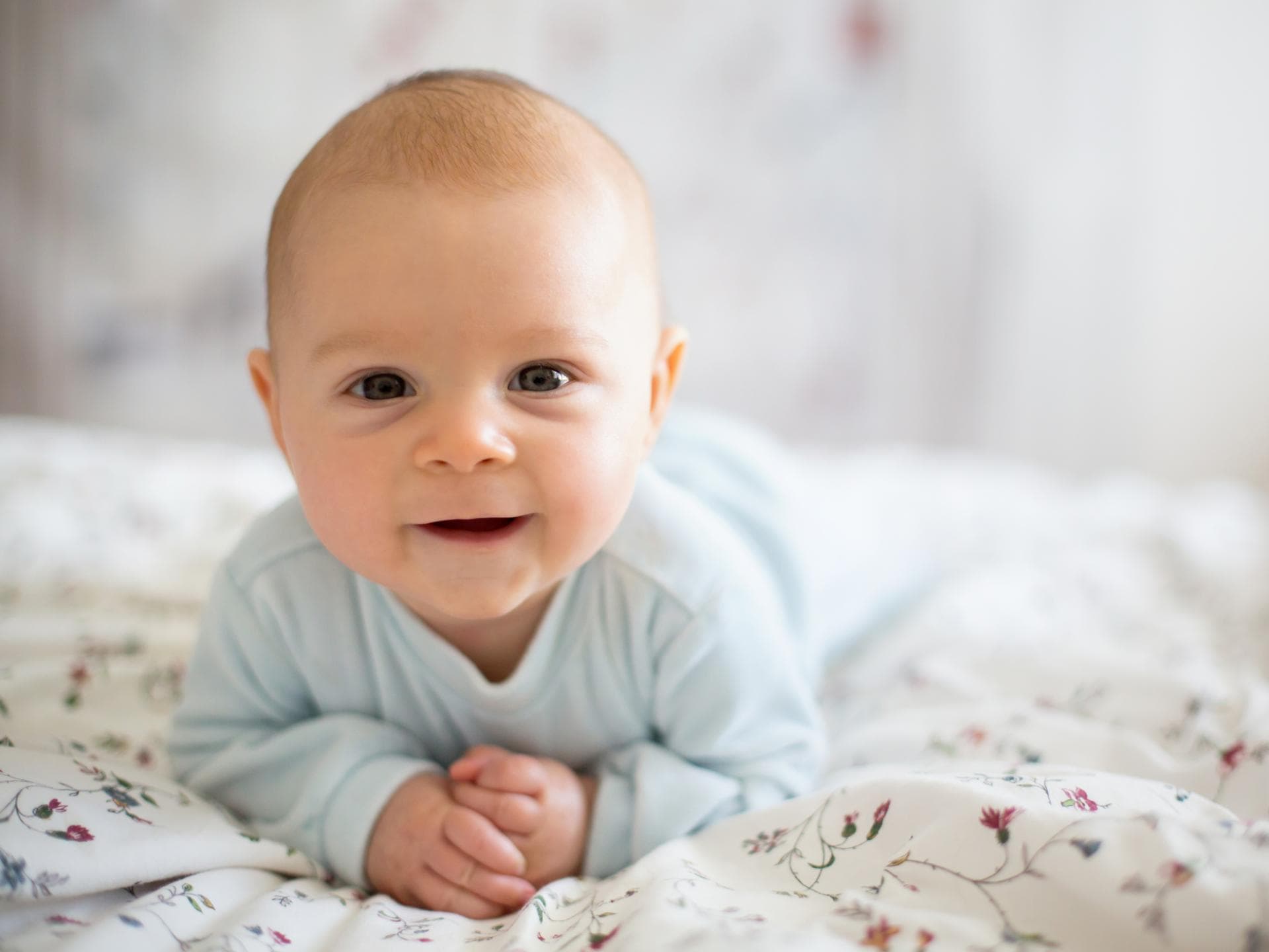 Talia, Thea, Tamika: Hier kommen Mädchennamen mit T. Ein Baby liegt auf dem Bauch und lächelt.