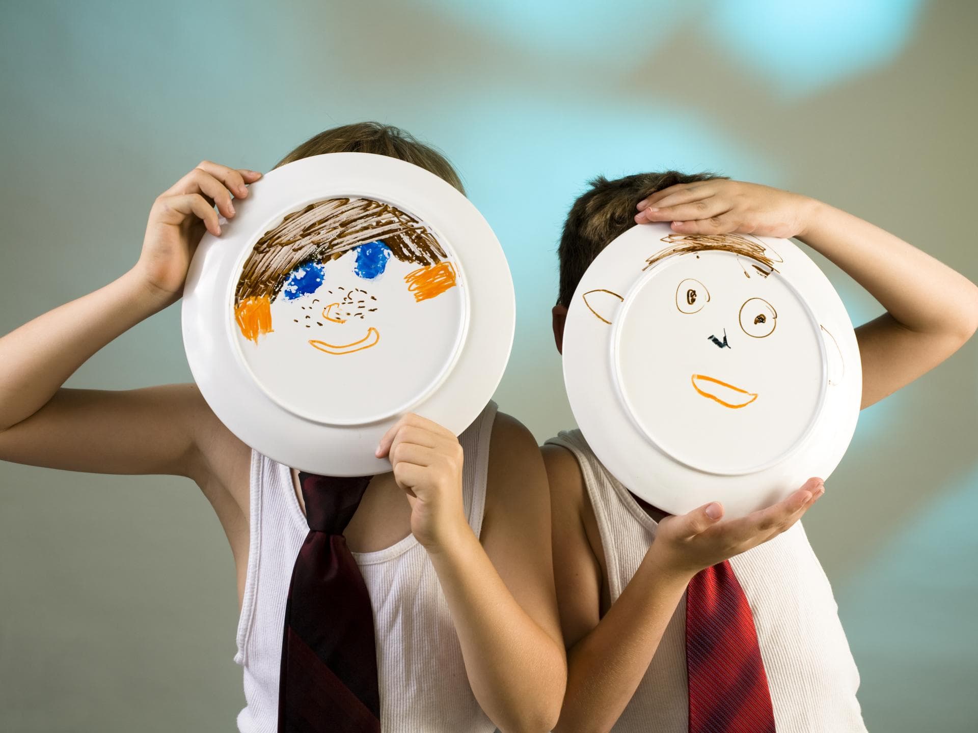 Melamin-Geschirr bitte nur in der Sandkiste verwenden. Zwei Jungen halten Teller hoch, auf die ein Gesicht gemalt ist.