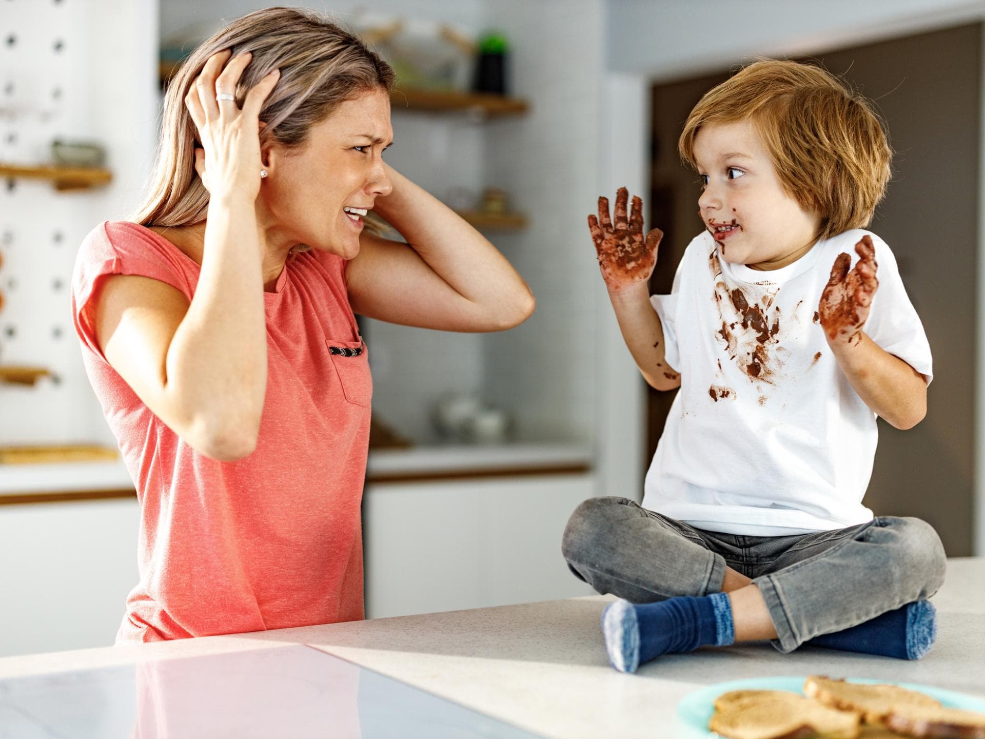Diese Mutter bereut das Muttersein. Mutter schlägt die Hände über dem Kopf zusammen, da ihr Sohn über und über mit Schokolade beschmiert ist.
