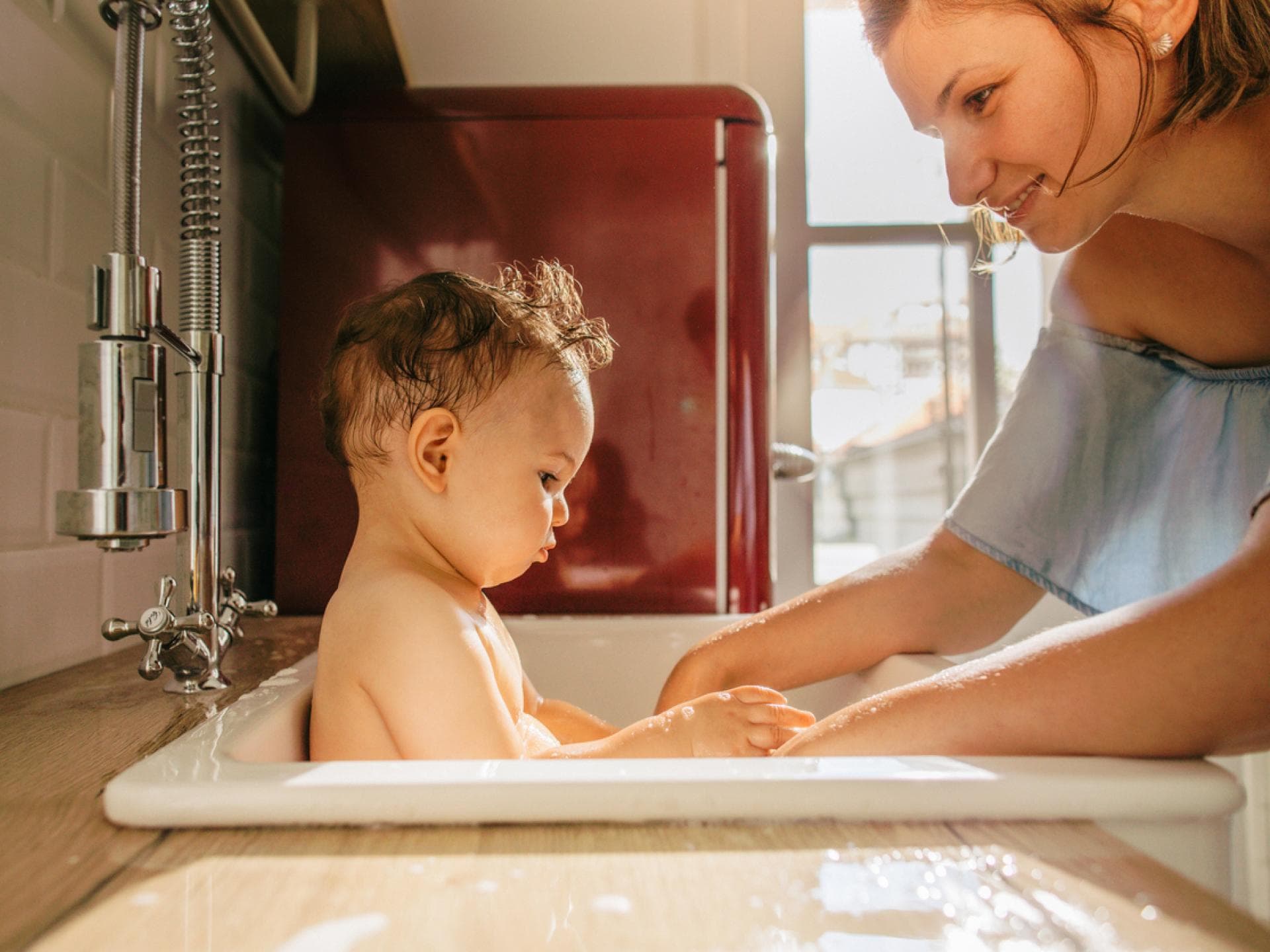 Eine junge Mutter badet ihr Baby im Waschbecken. Eine junge Mutter badet ihr Baby im Waschbecken.