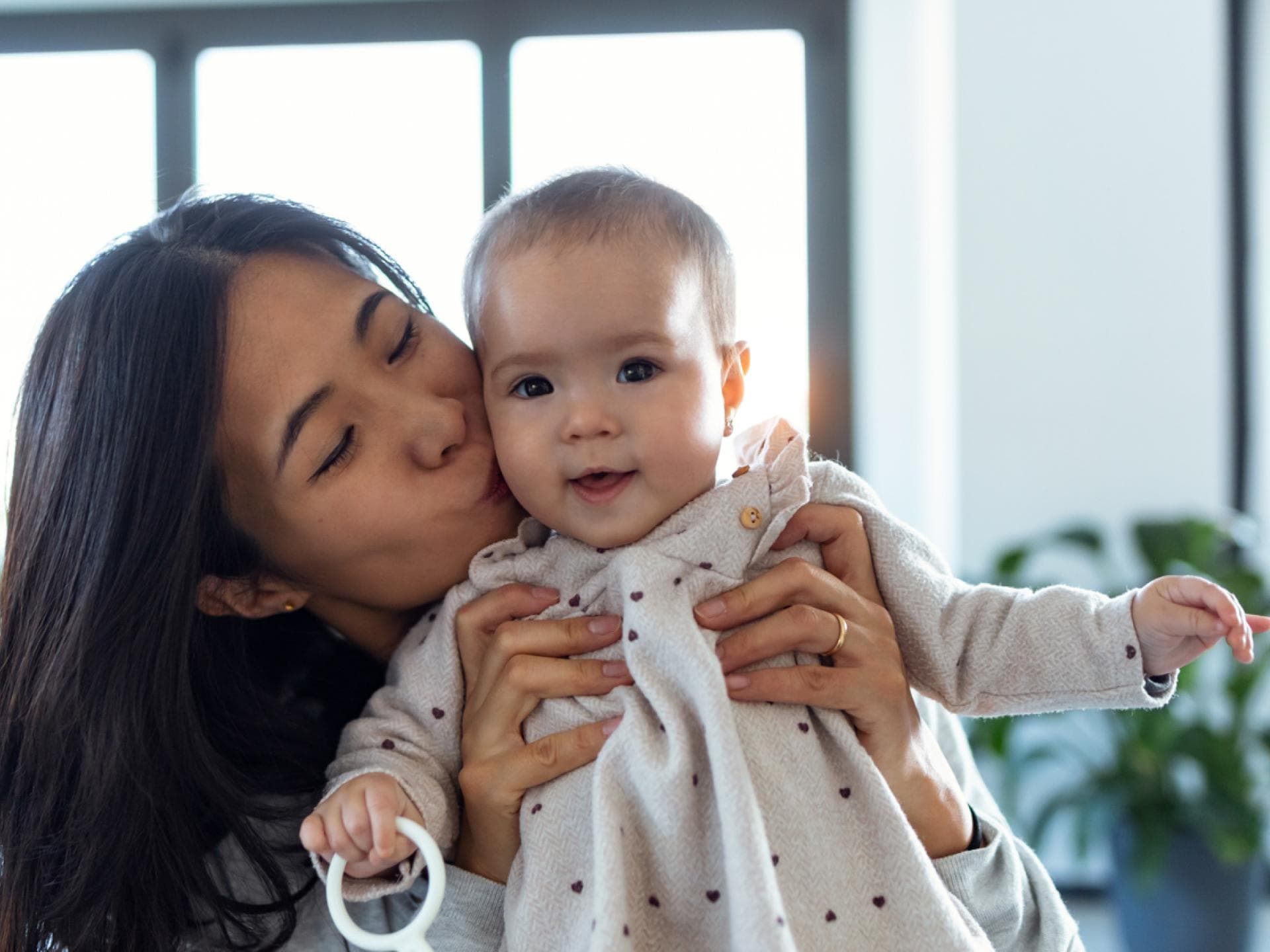 Eine asiatische Mutter hält ihr Baby-Mädchen hoch und küsst es zärtlich auf die Wange. Eine asiatische Mutter hält ihr Baby-Mädchen hoch und küsst es zärtlich auf die Wange.