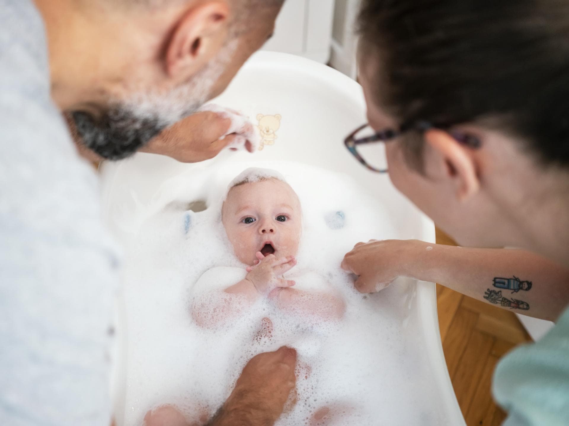 Eltern baden ihr Baby in einer Babybadewanne mit viel Badezusatz und Schaum. Eltern baden ihr Baby in einer Babybadewanne mit viel Badezusatz und Schaum.