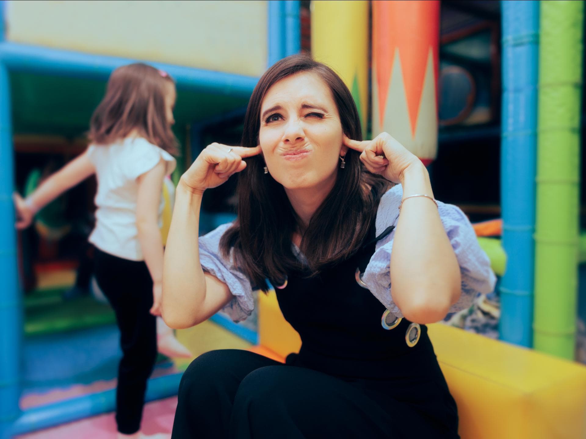 Frau hält sich auf einem Spielplatz die Ohren zu