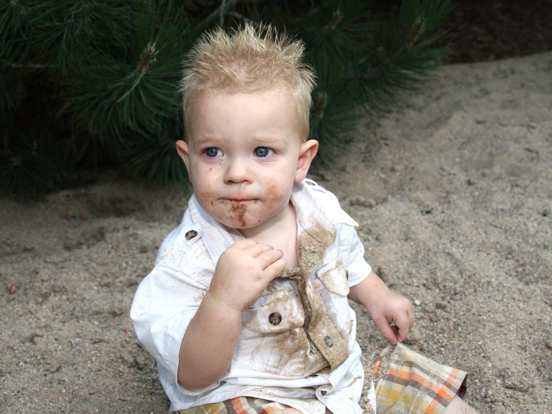 Kinder essen auf dem Spielplatz oft Sand. Ein mit Sand verschmiertes Kind