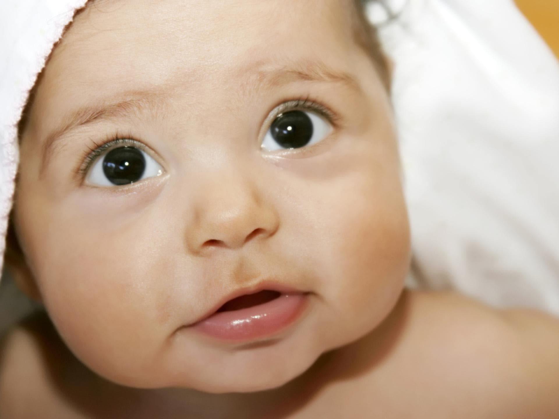 Niedliches Baby schaut eingewickelt in ein Handtuch mit Dackelblick in die Kamera. Niedliches Baby schaut eingewickelt in ein Handtuch mit Dackelblick in die Kamera.