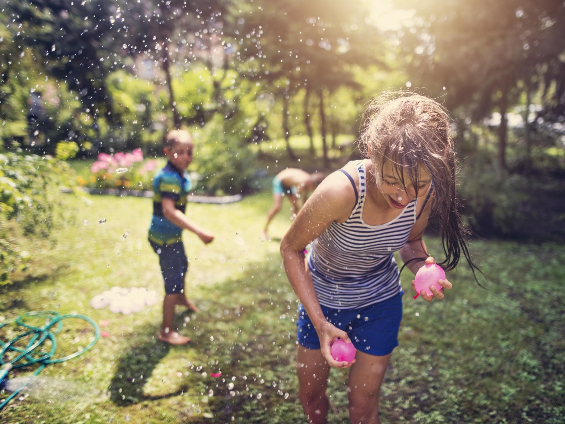 Zwei Kinder bewerfen sich im Garten mit Wasserbomben.