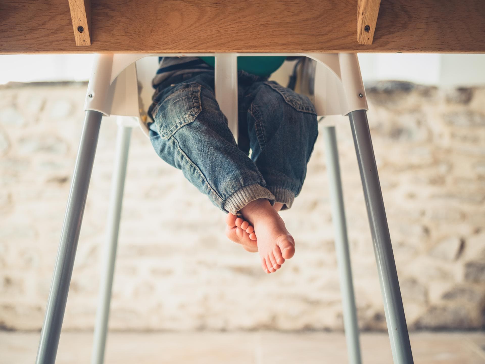 Kinderbeine unterm Tisch im Hochstuhl