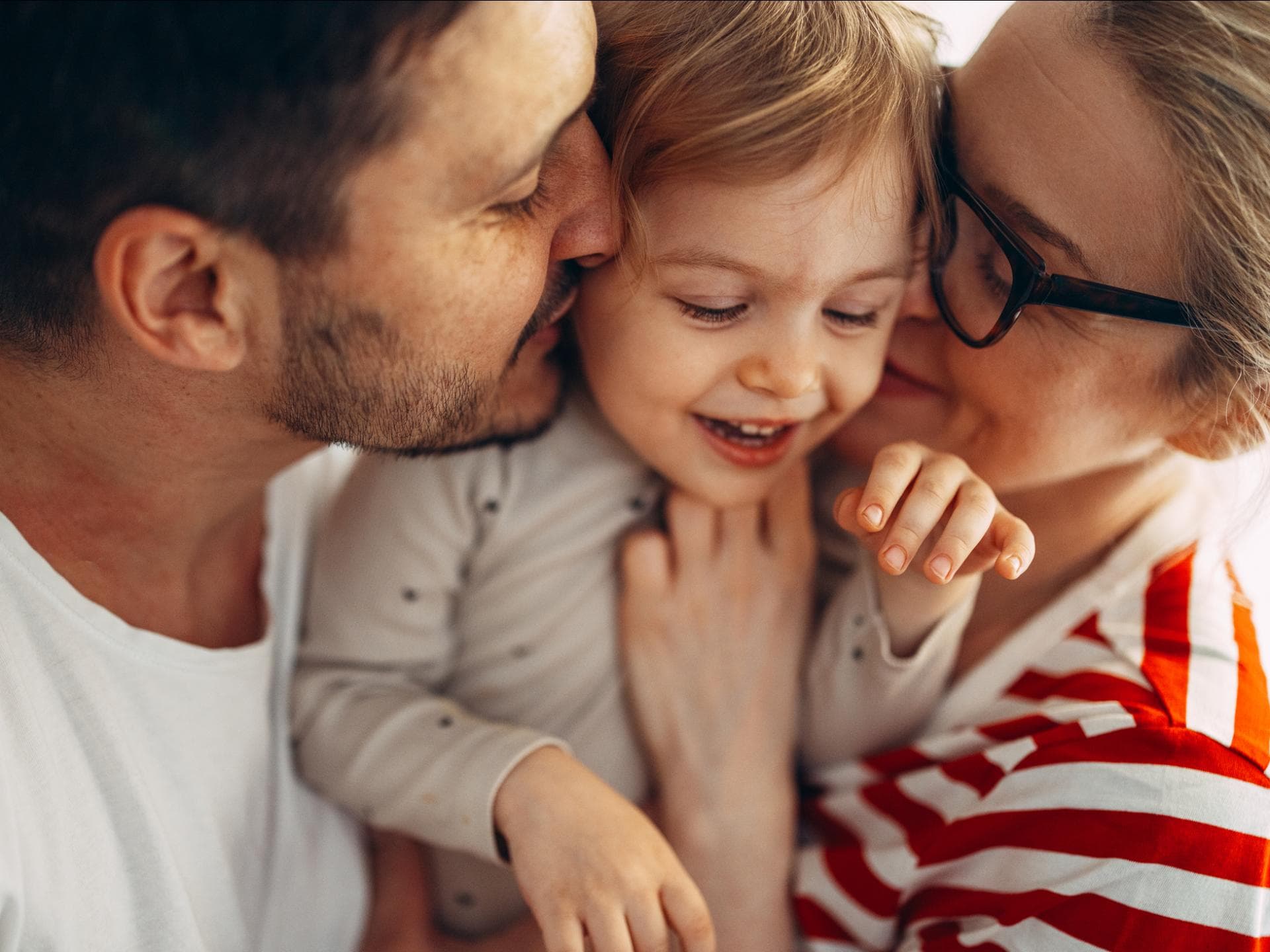 Glückliche Eltern kuscheln mit ihrer Tochter.