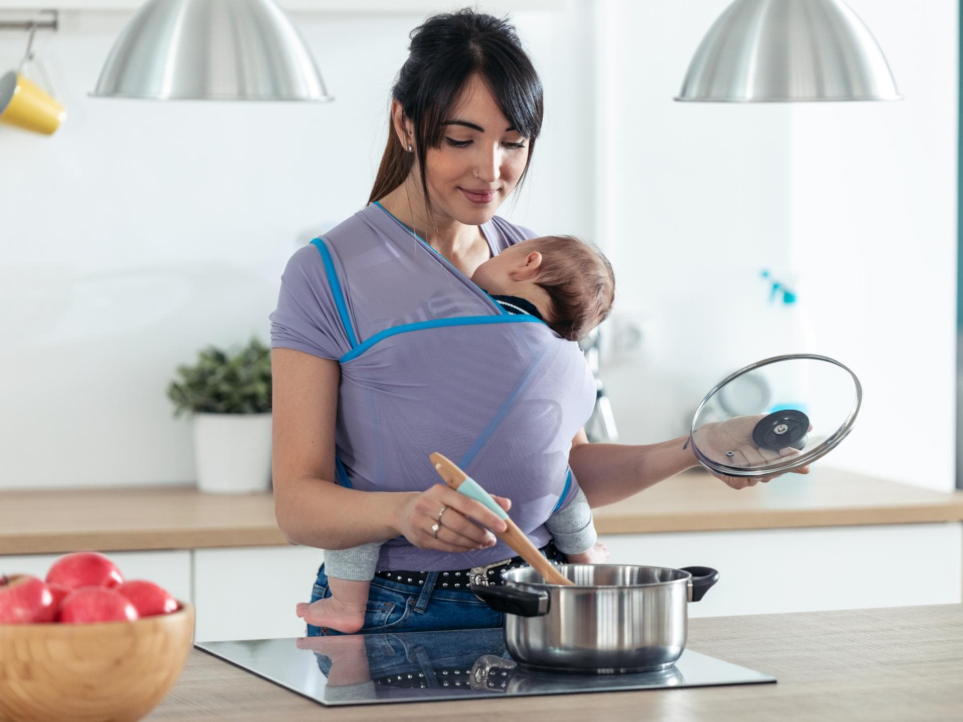 Mama mit Baby in Babytrage beim Kochen Mama mit Baby in Babytrage beim Kochen