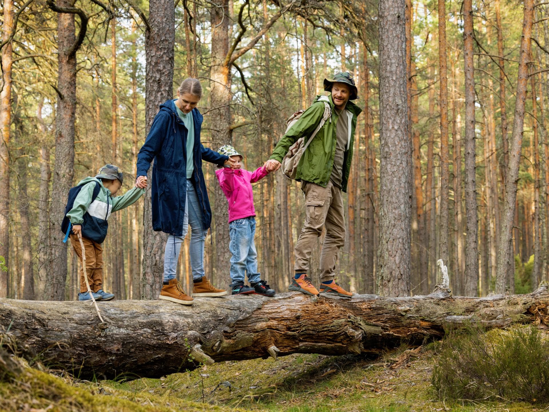 Familie läuft auf Baumstamm im Wald.