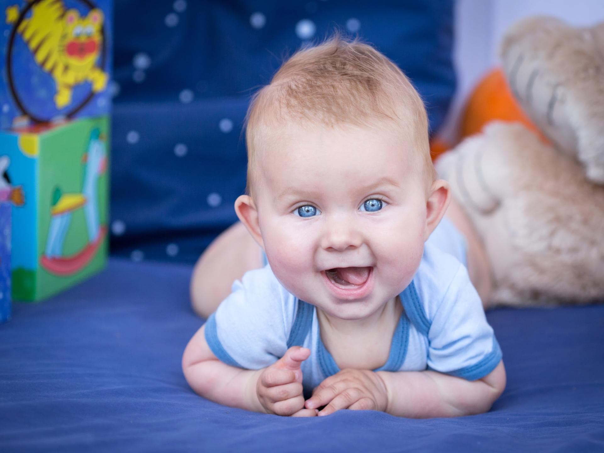 Süßer Babyjunge liegt auf dem Bauch und lächelt in die Kamera. 