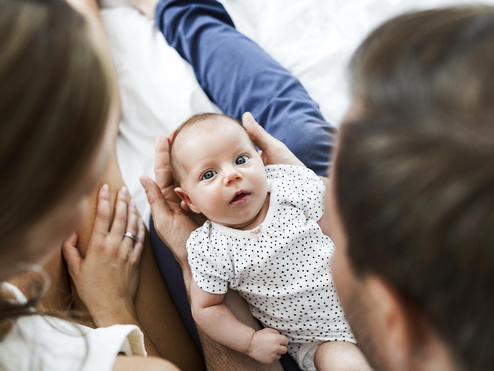 Mutter, Vater und Baby auf einem weißen Bett.