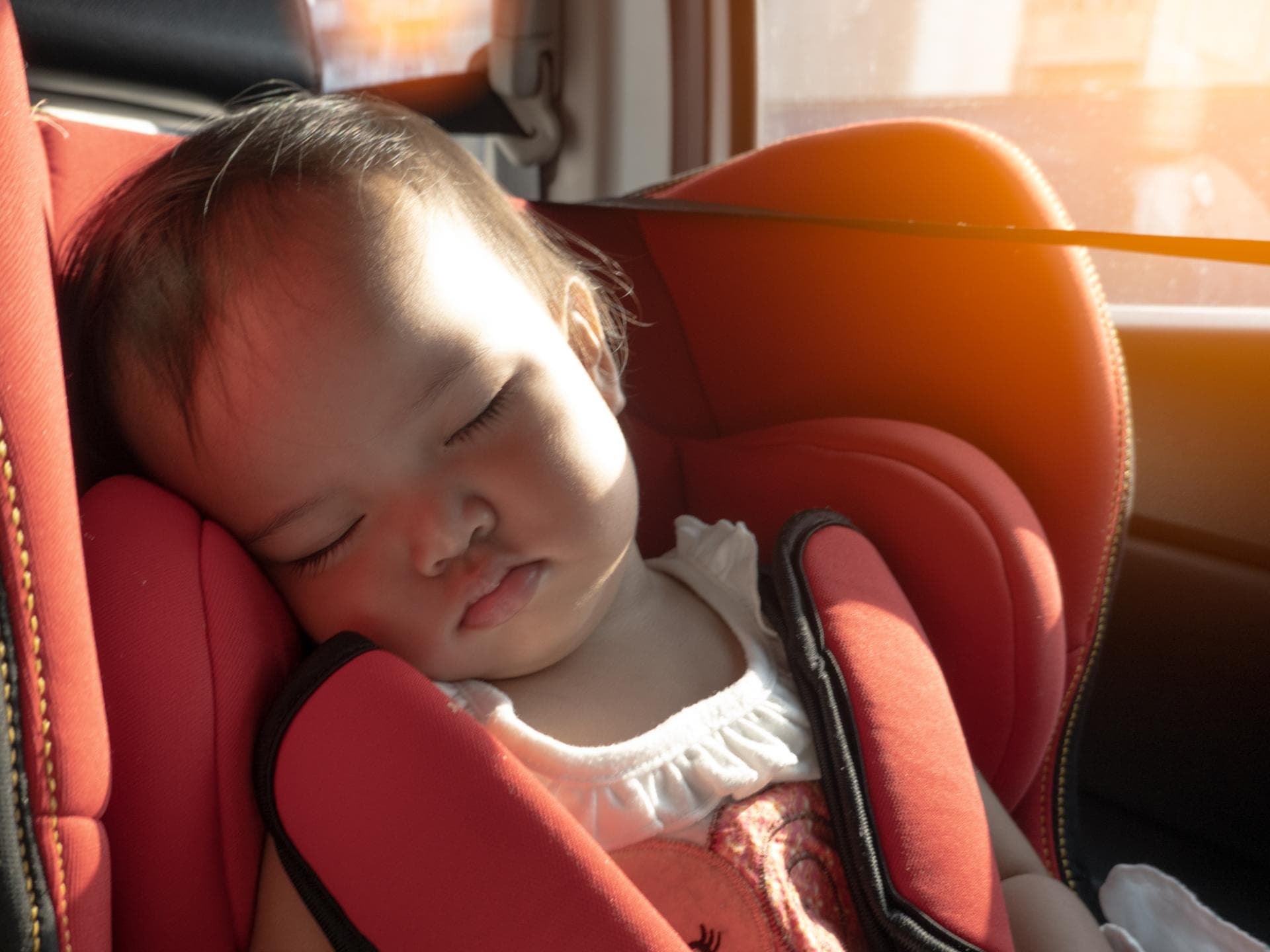Ein Baby sitzt im Kindersitz des Autos, während die Sonne hereinscheint.