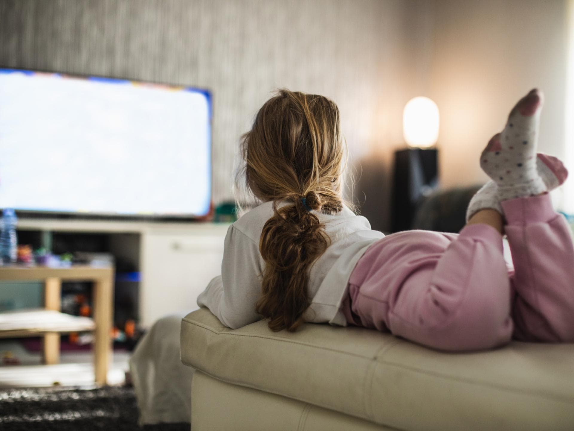 Ein Mädchen liegt auf dem Sofa und schaut eine Kinderserie. Ein Mädchen liegt auf dem Sofa und schaut eine Kinderserie.