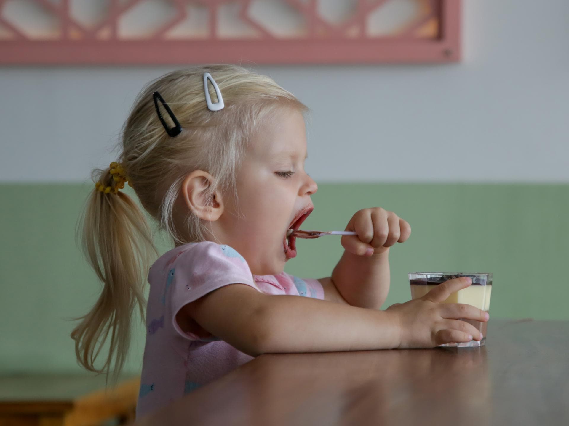 Kleines Mädchen löffelt Dessert. 