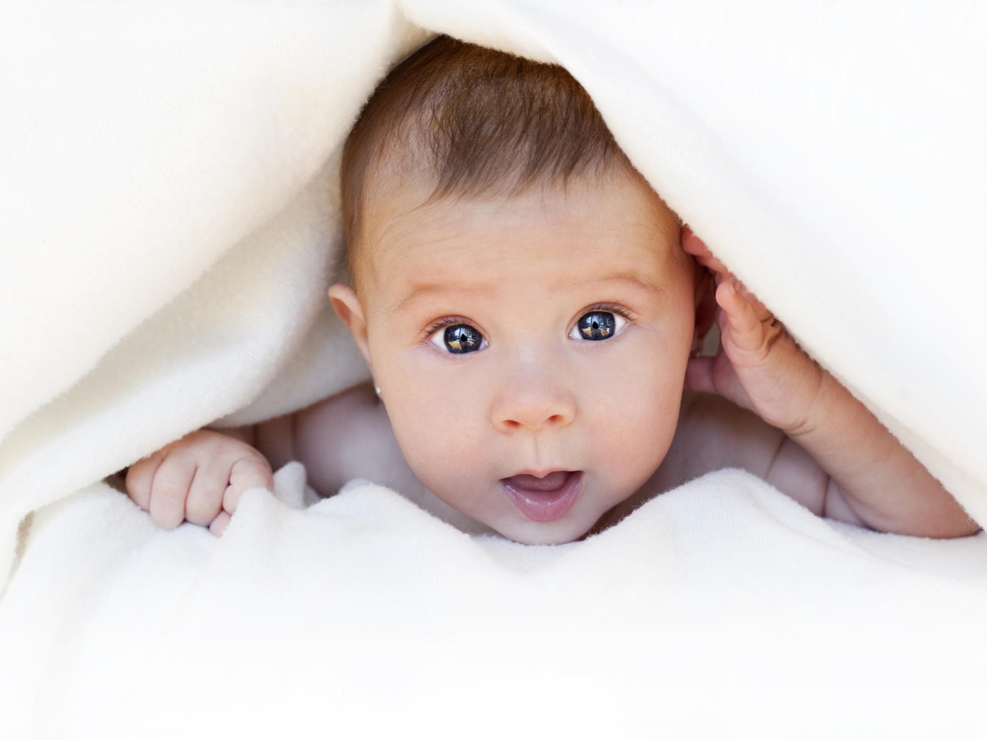 Baby guckt unter weißer Decke hervor.