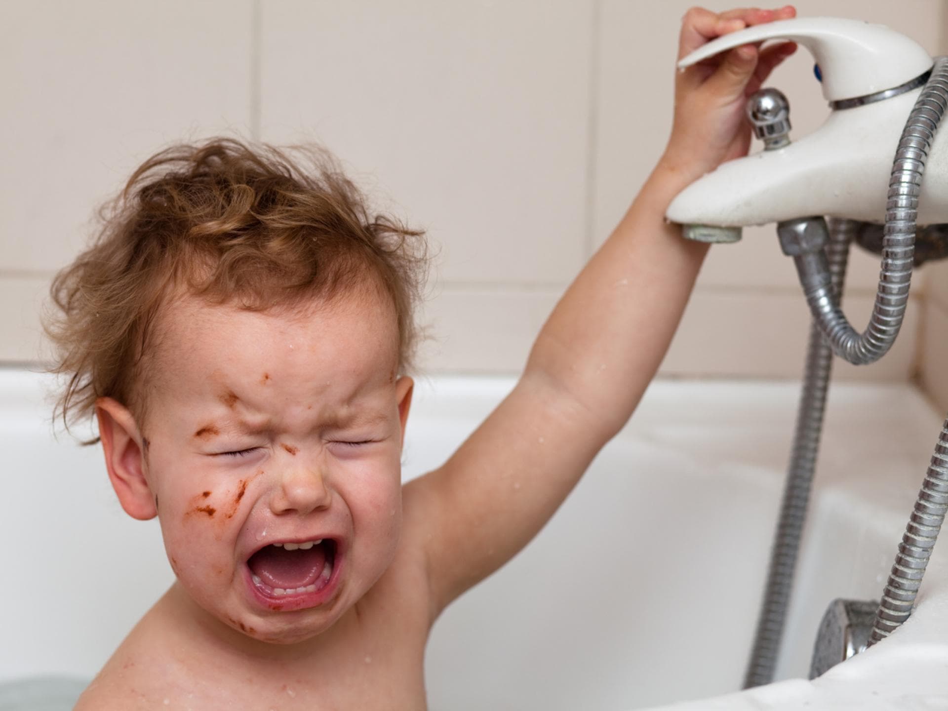 Ein Baby schreit beim Baden in der Badewanne und kneift dabei die Augen zu.