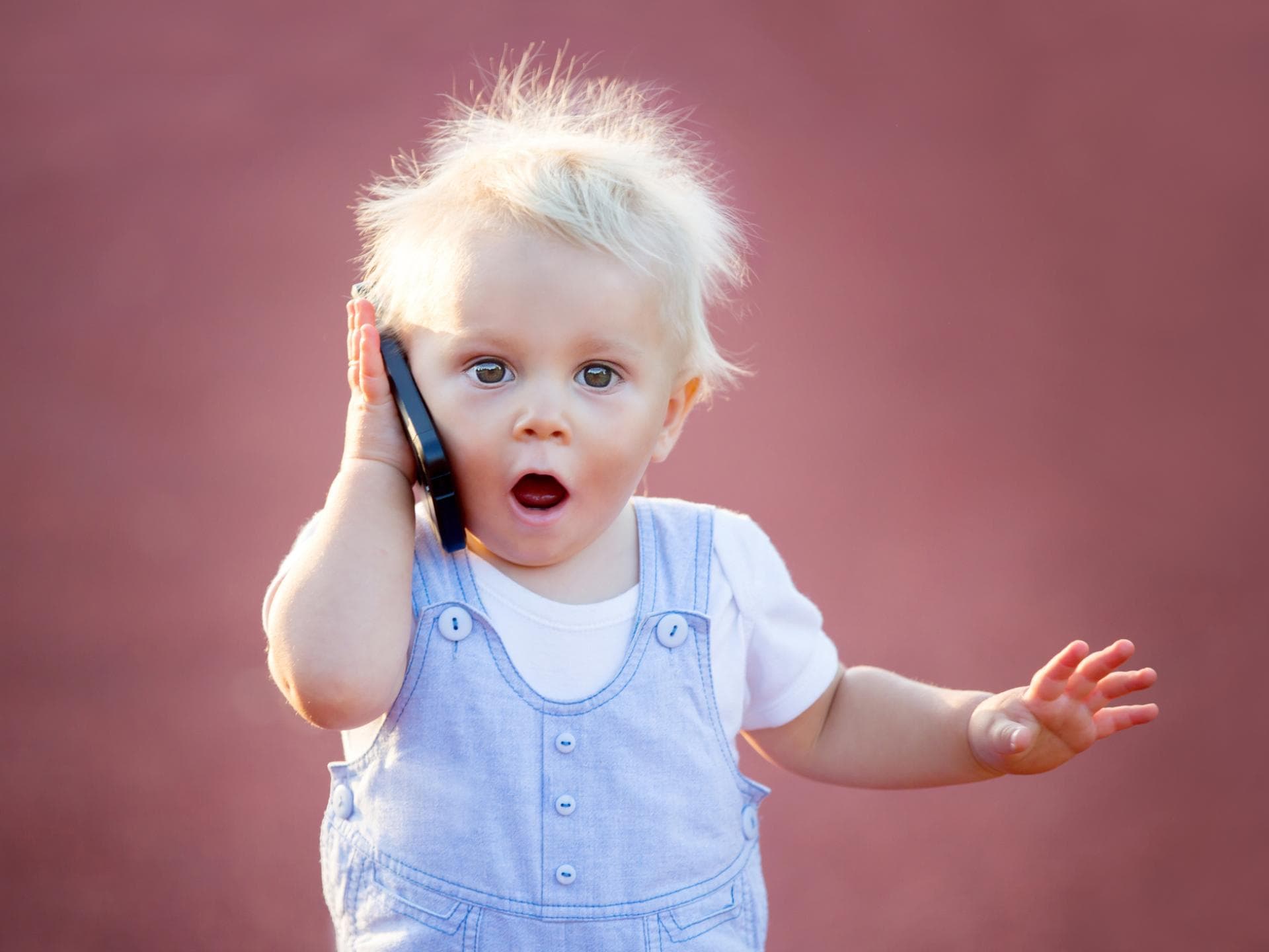 Ein kleiner Baby-Junge hält ein Handy in der Hand und schaut schockiert.