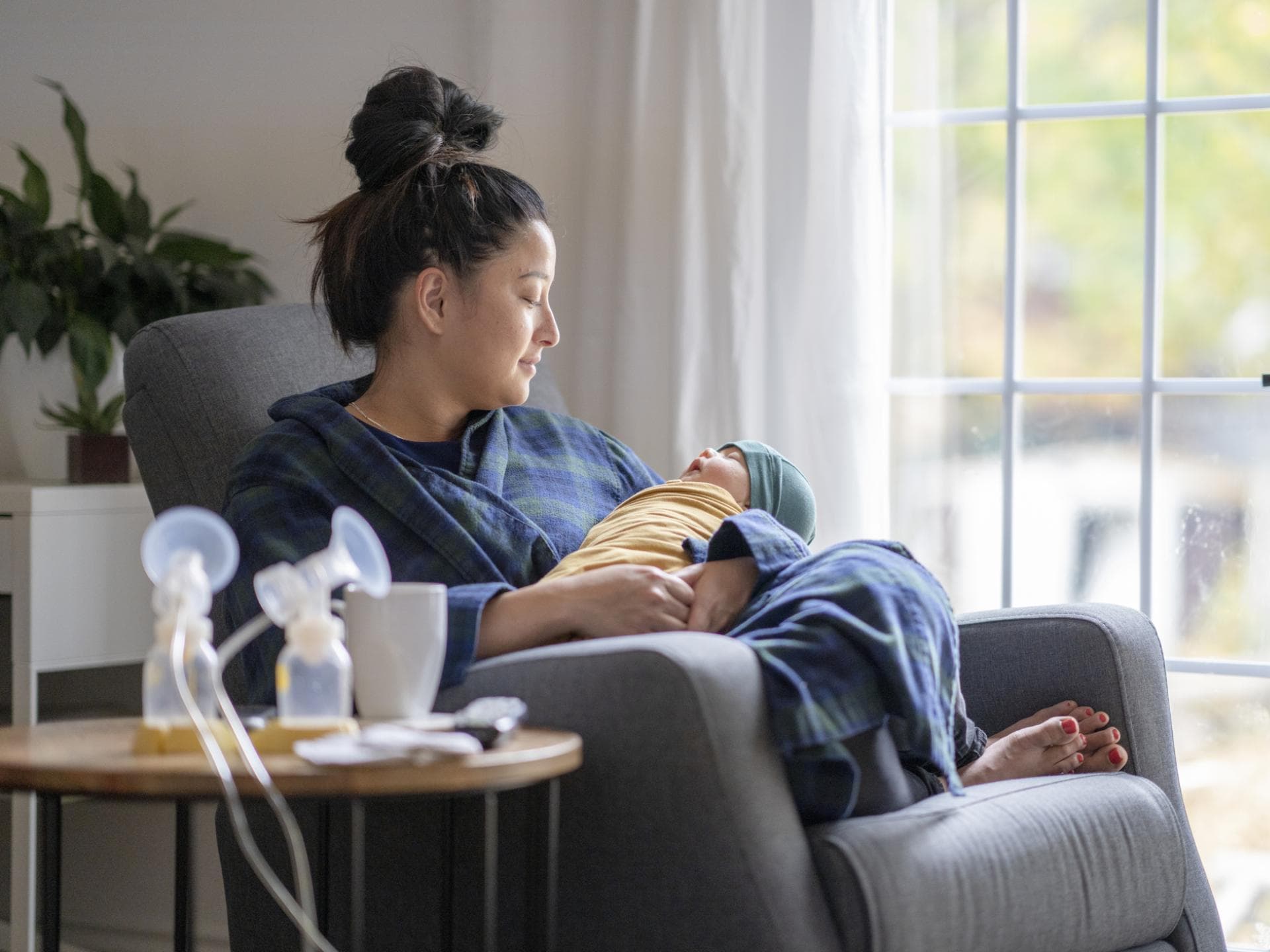 Eine Mama sitzt mit ihrem Baby und einer Milchpumpe auf dem Sofa. Eine Mama sitzt mit ihrem Baby und einer Milchpumpe auf dem Sofa.