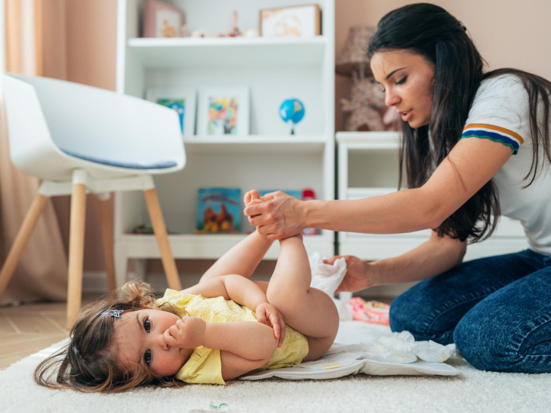 Junge Mutter wickelt ihr Baby auf dem Boden mit Feuchttüchern