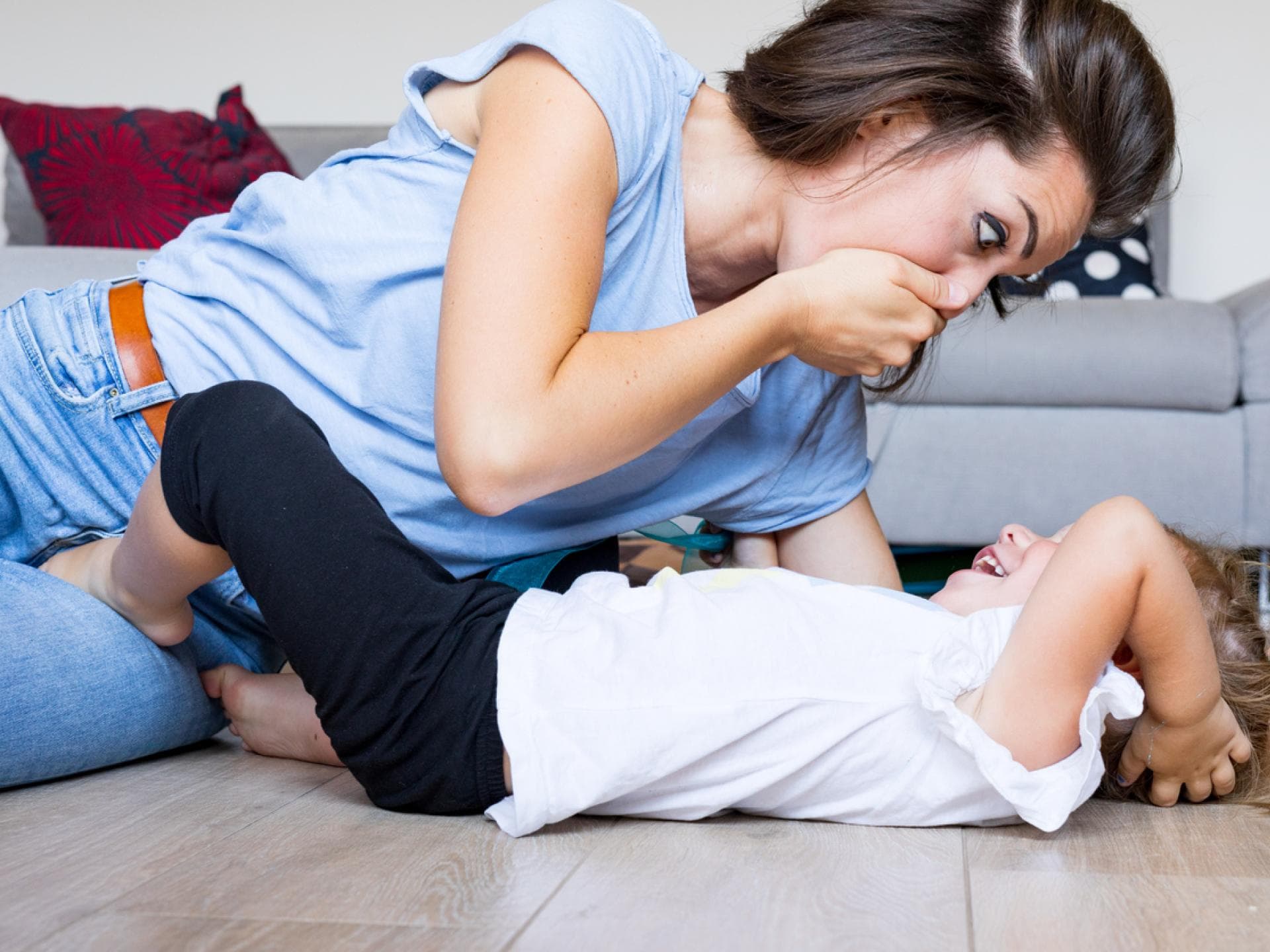 Eine Mutter spielt mit ihrer Tochter und hält sich die Hand vor den Mund. Eine Mutter spielt mit ihrer Tochter und hält sich die Hand vor den Mund.