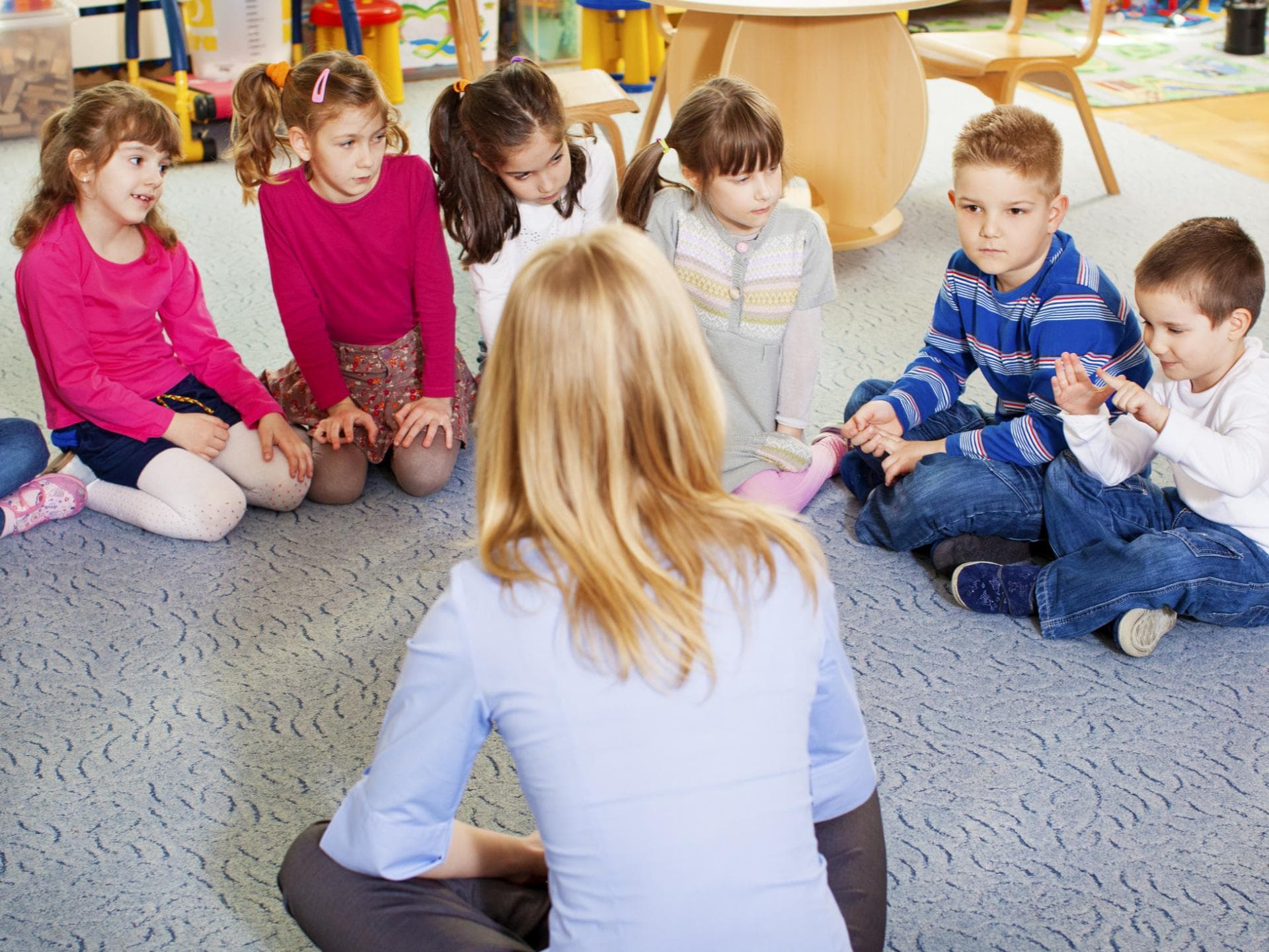 Kinder und Erzieherin sitzen im Kreis.