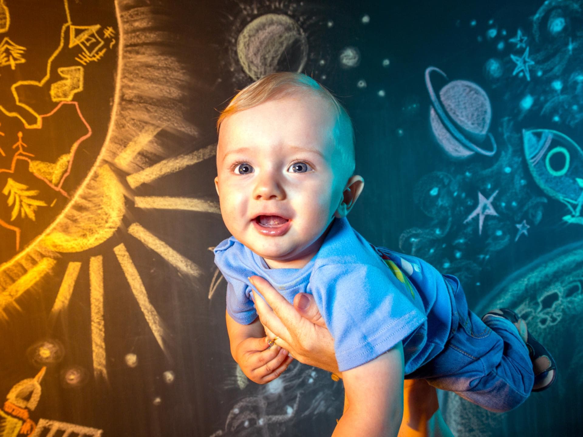 Baby schwebt auf den Händen der Eltern durch den "Weltraum"