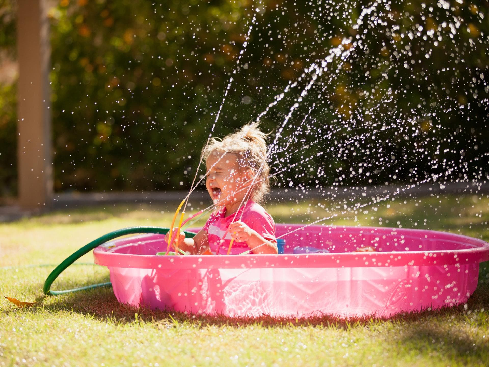 Wasserspielzeug Kleines Mädchen spielt in einem Plantschbecken mit einem Wasserspielzeug.