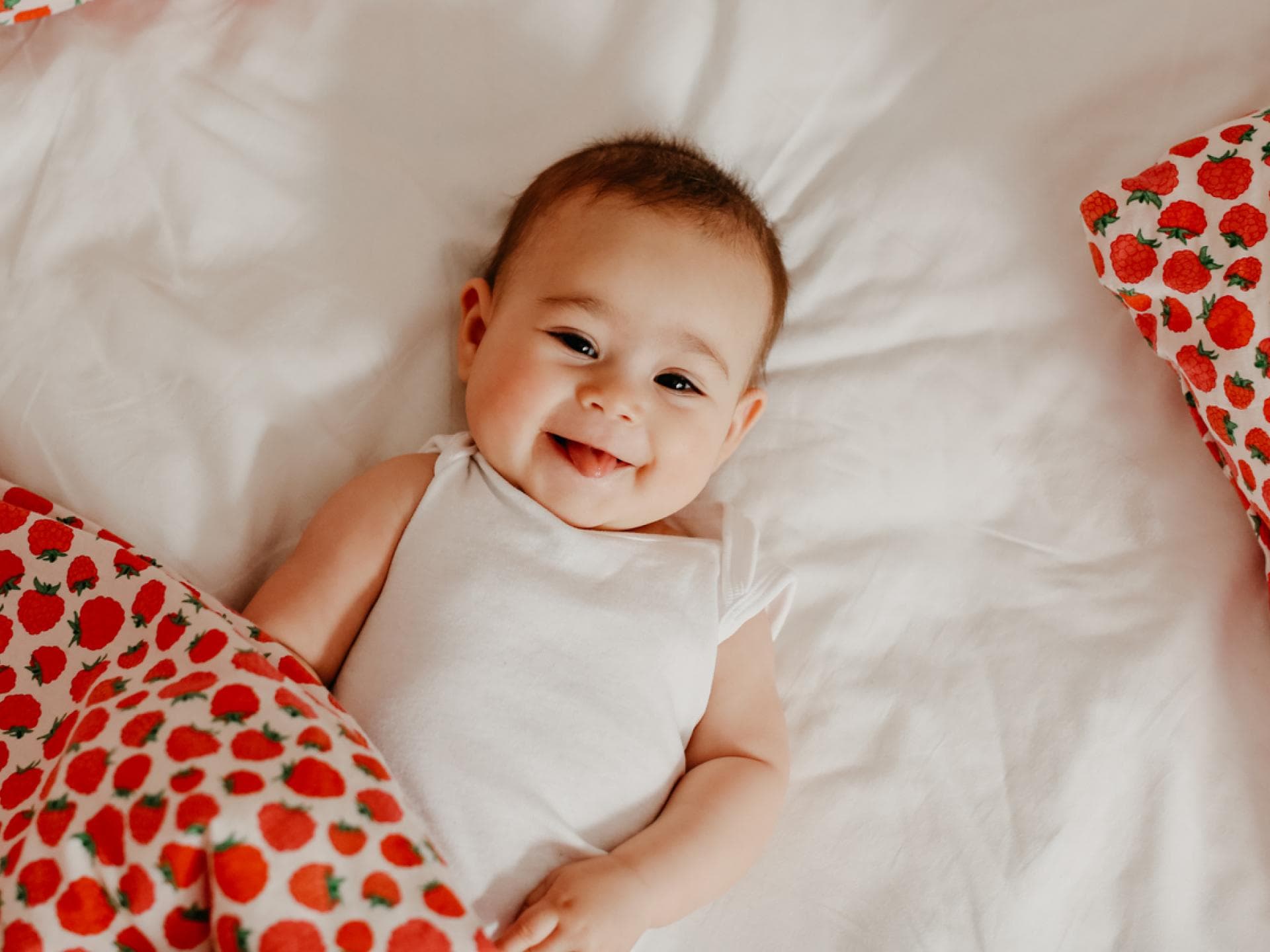 Kleines Baby-Mädchen lacht frech in die Kamera und liegt auf dem Boden.